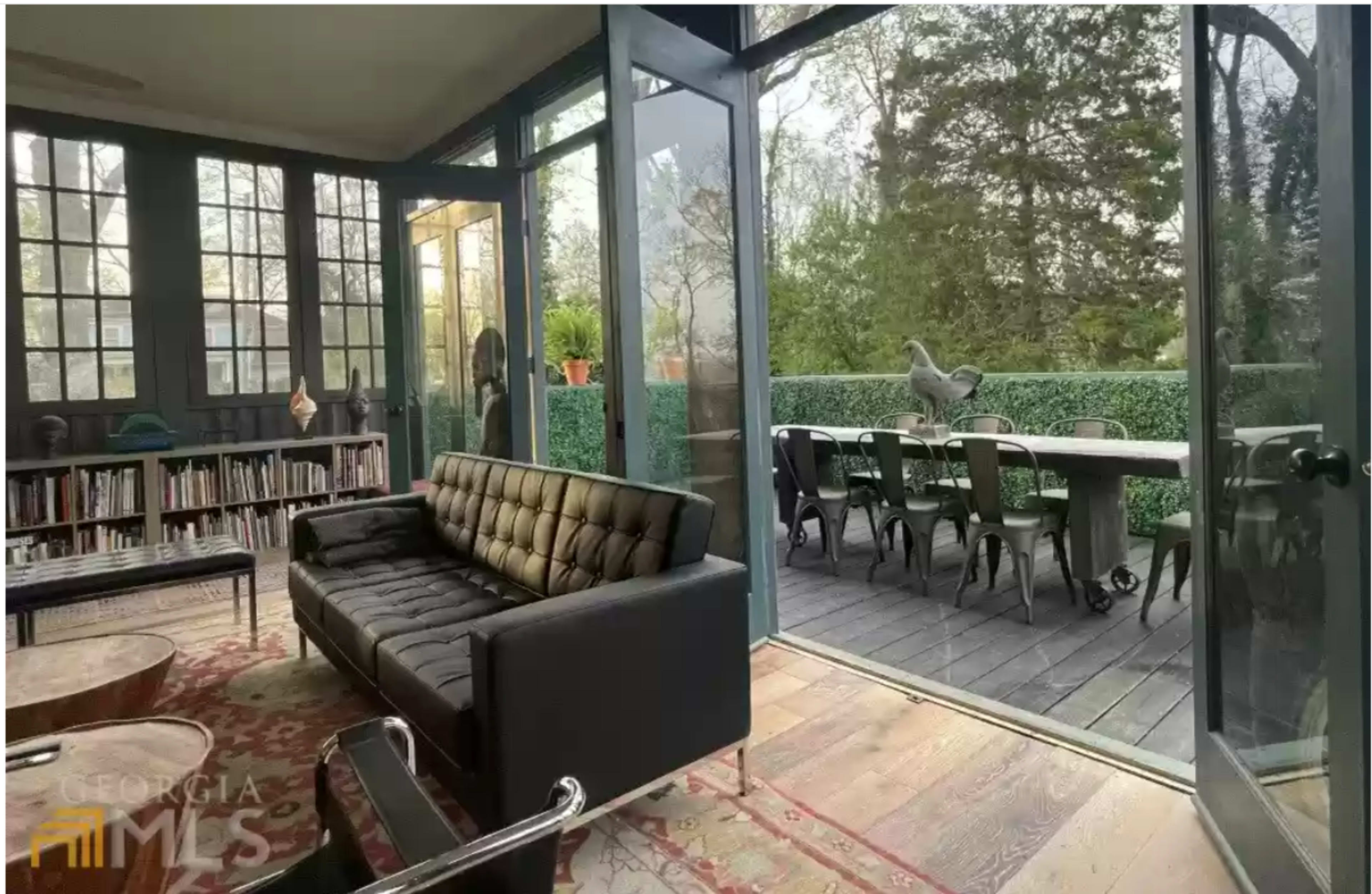 A modern, glass-enclosed living space with a black, tufted sofa facing a patio area filled with outdoor dining furniture.
