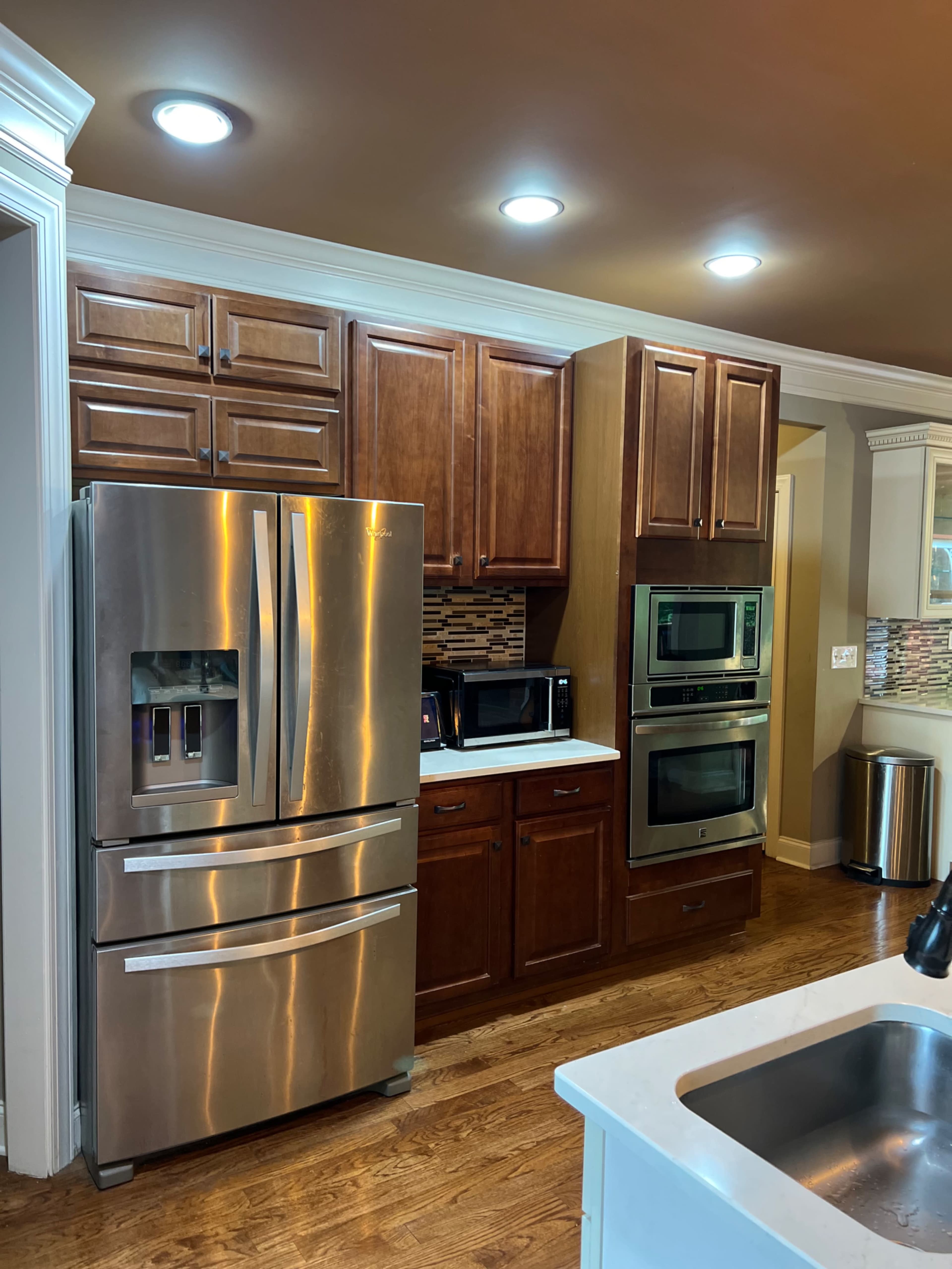 The image shows a kitchen with wood cabinetry, stainless steel appliances, and a countertop sink.
