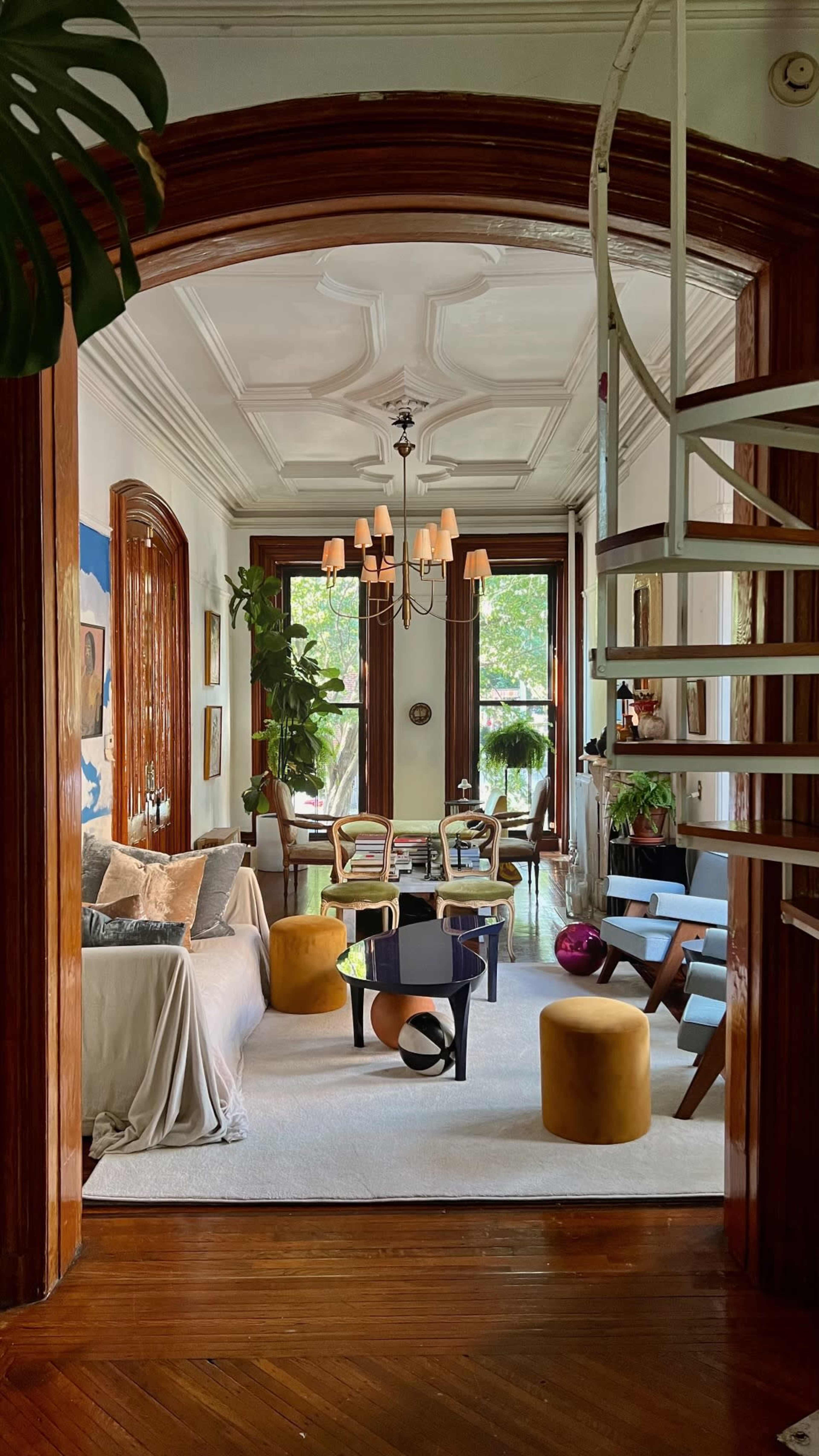 The image shows a spacious, well-lit living area connected to a dining space, featuring a spiral staircase and a mix of modern and classic furniture.