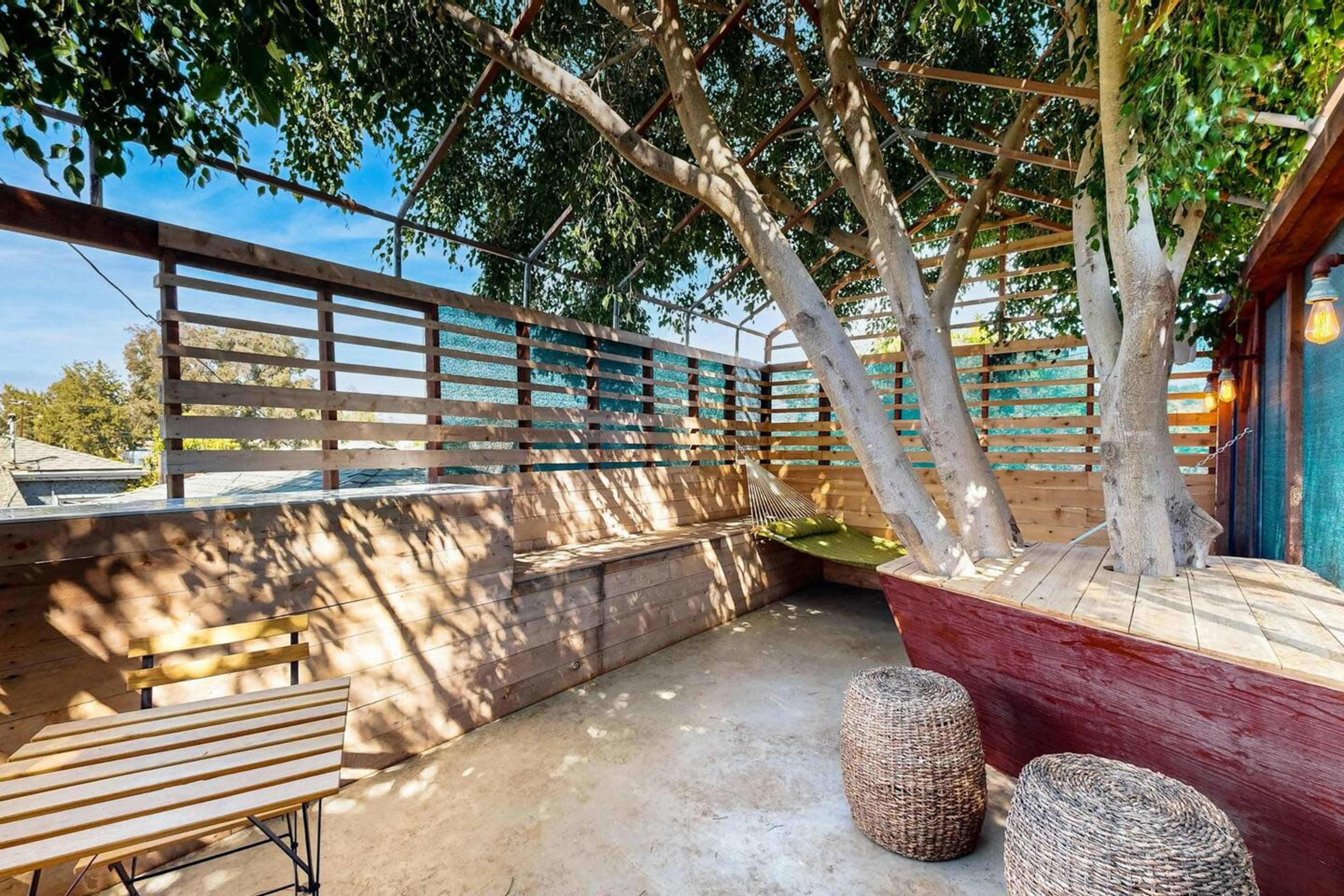 A wooden deck area features a large tree, seating arrangements, and a fenced enclosure for shade.