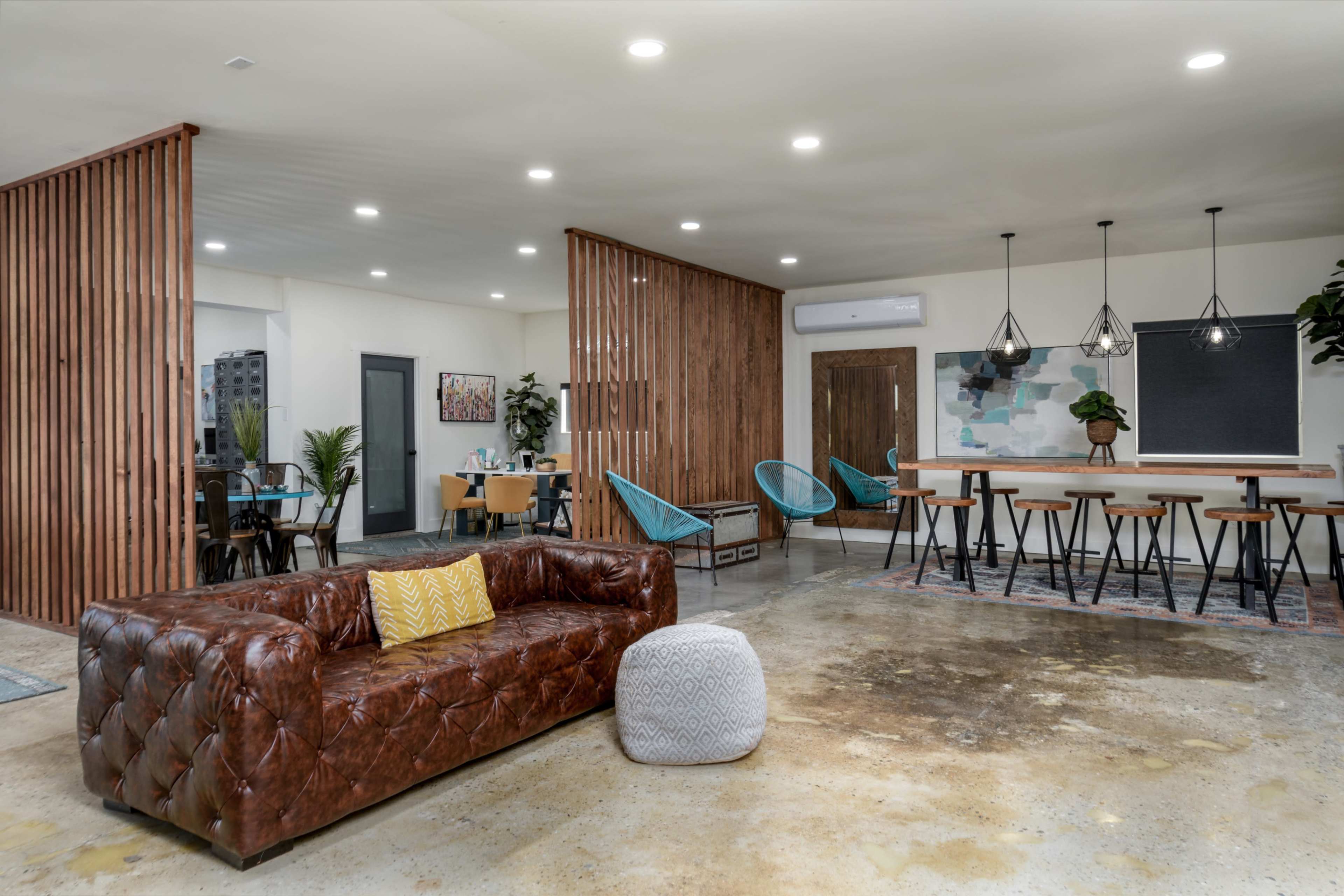 A modern open space with a brown leather couch, light wood partitions, dining tables, and blue chairs.
