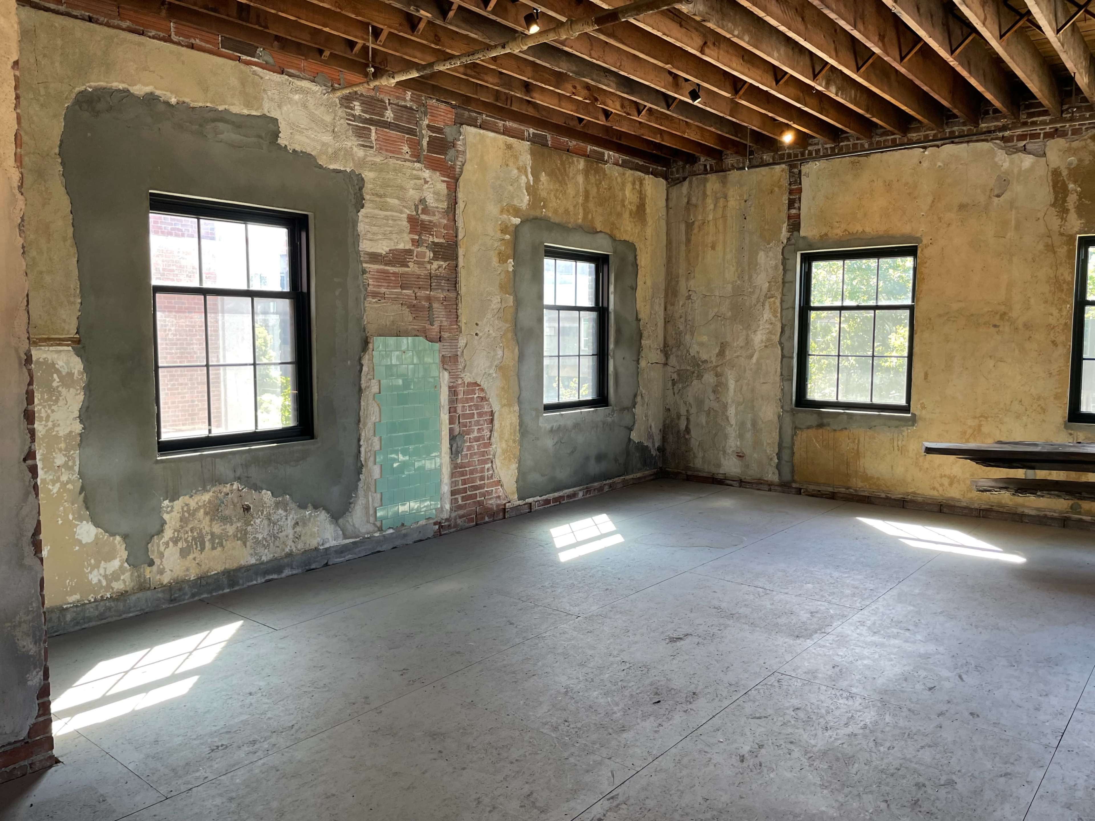 An empty room with exposed brick walls, peeling plaster, and two windows that let in natural light.