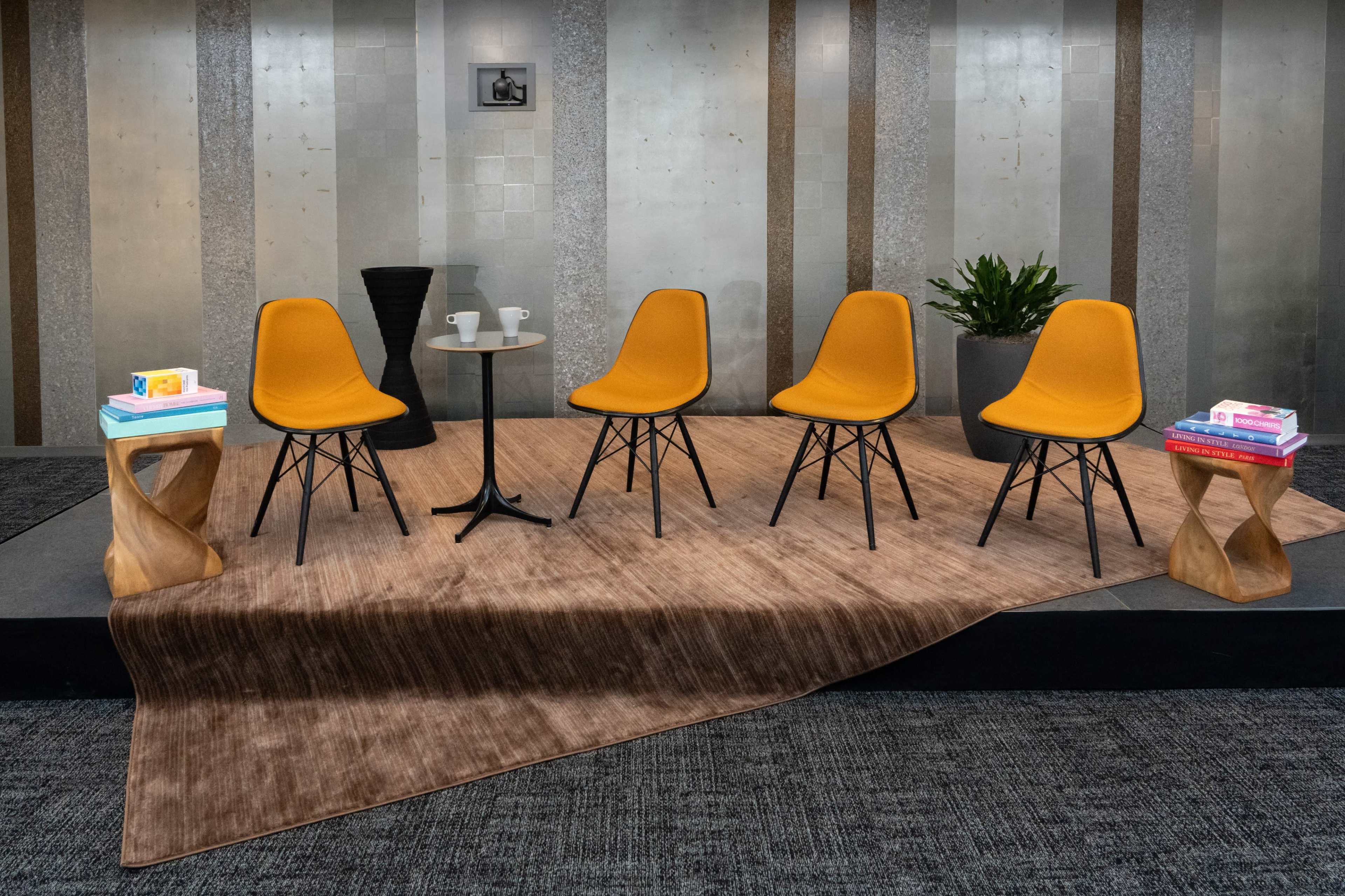 A set of four yellow chairs is arranged around a small table on a textured rug in a modern interior space.