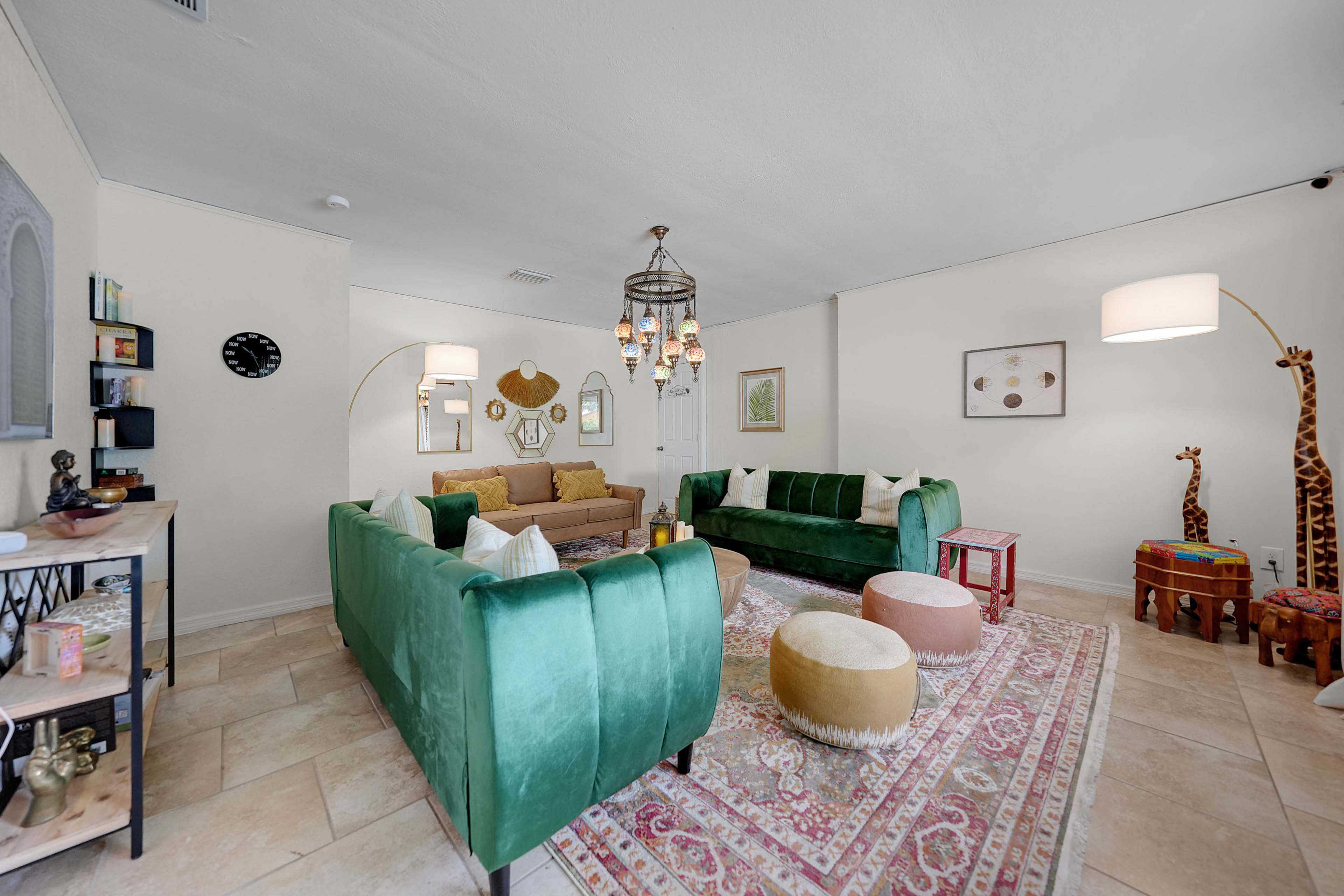 The living room features green velvet sofas, a patterned area rug, decorative lamps, and various artwork on the walls.