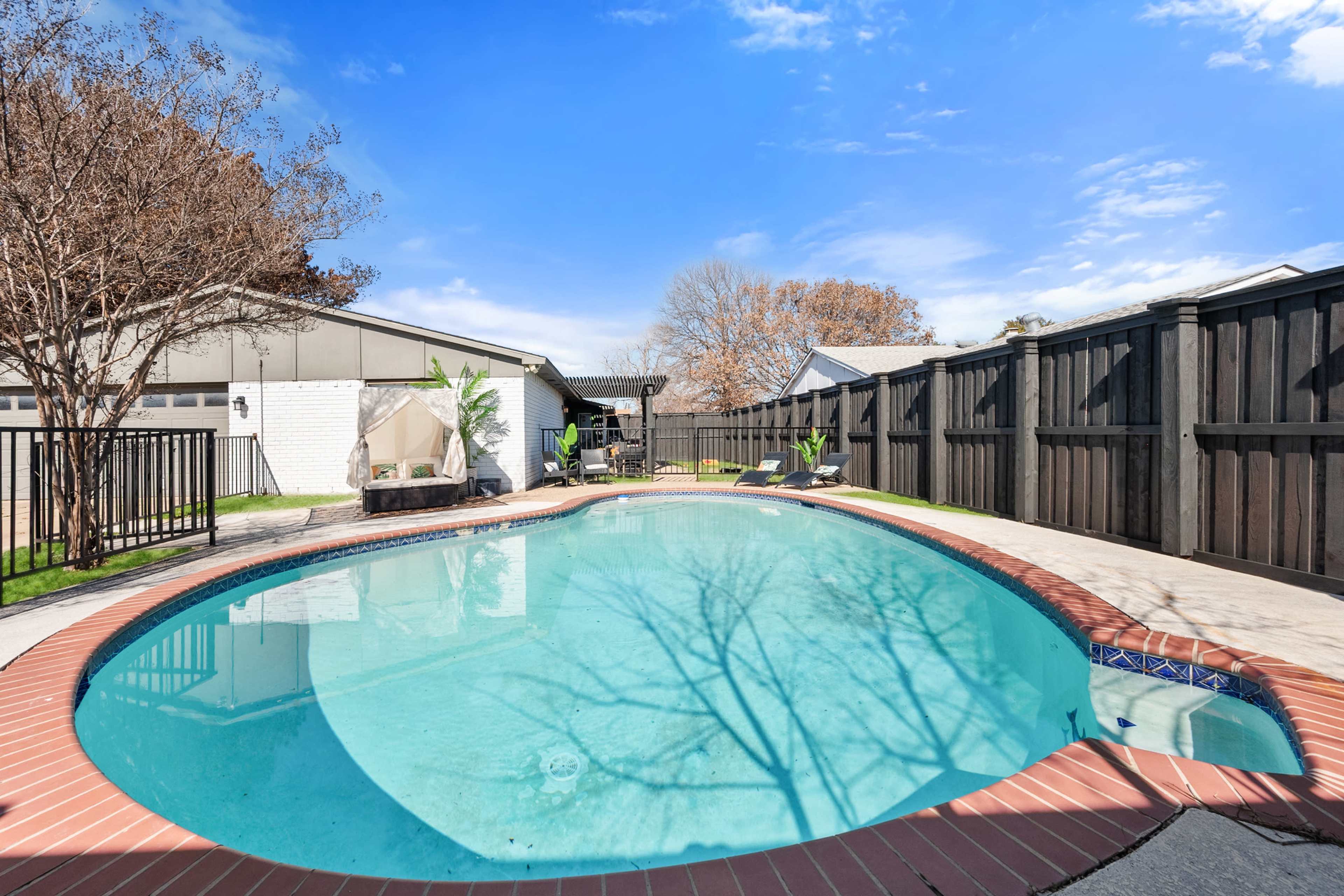 A backyard features a swimming pool surrounded by a concrete patio and wooden fencing.