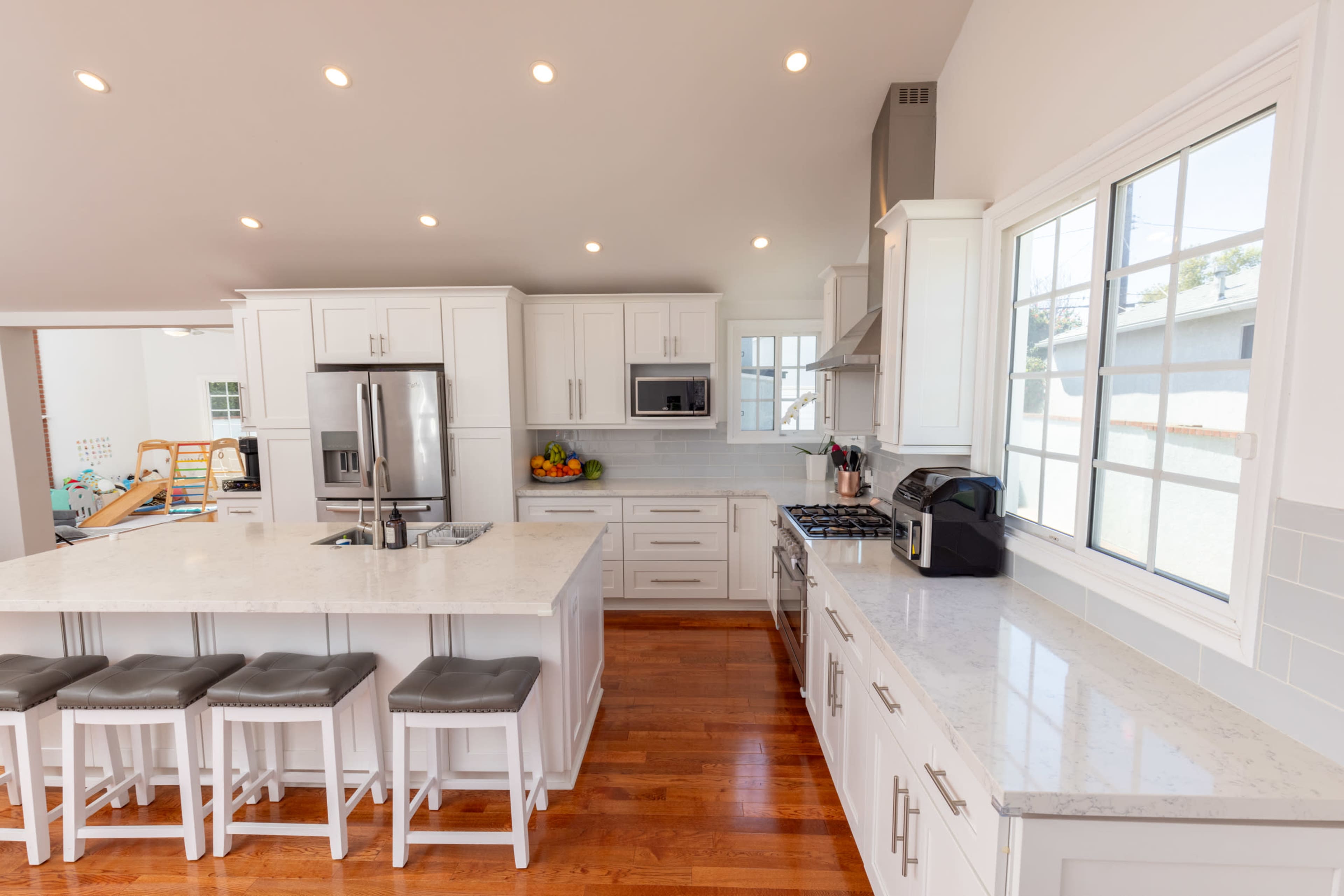 The image shows a modern kitchen with white cabinets, a large island, and stainless steel appliances.