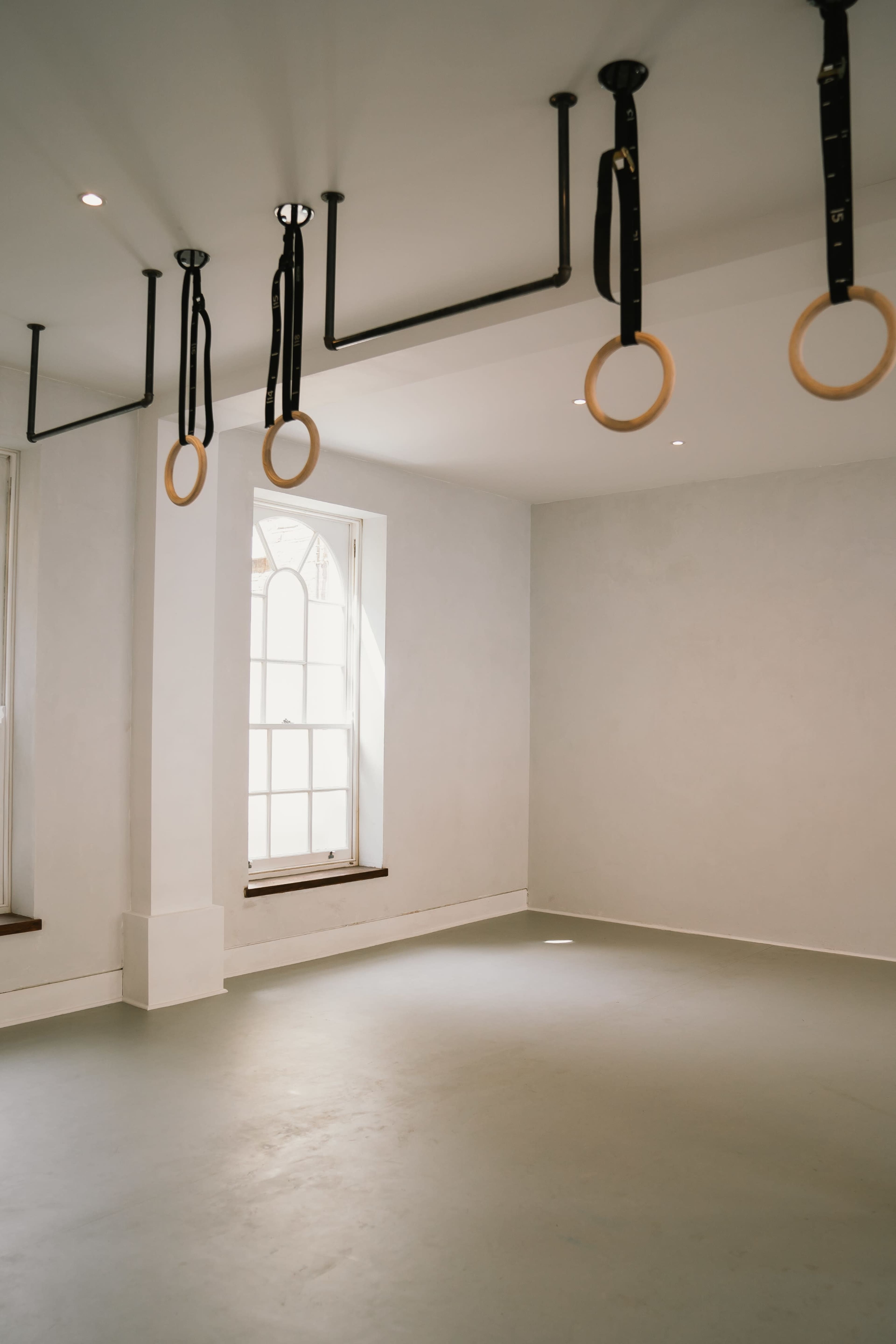 An empty room with a smooth gray floor, two large windows, and gymnastic rings hanging from the ceiling.