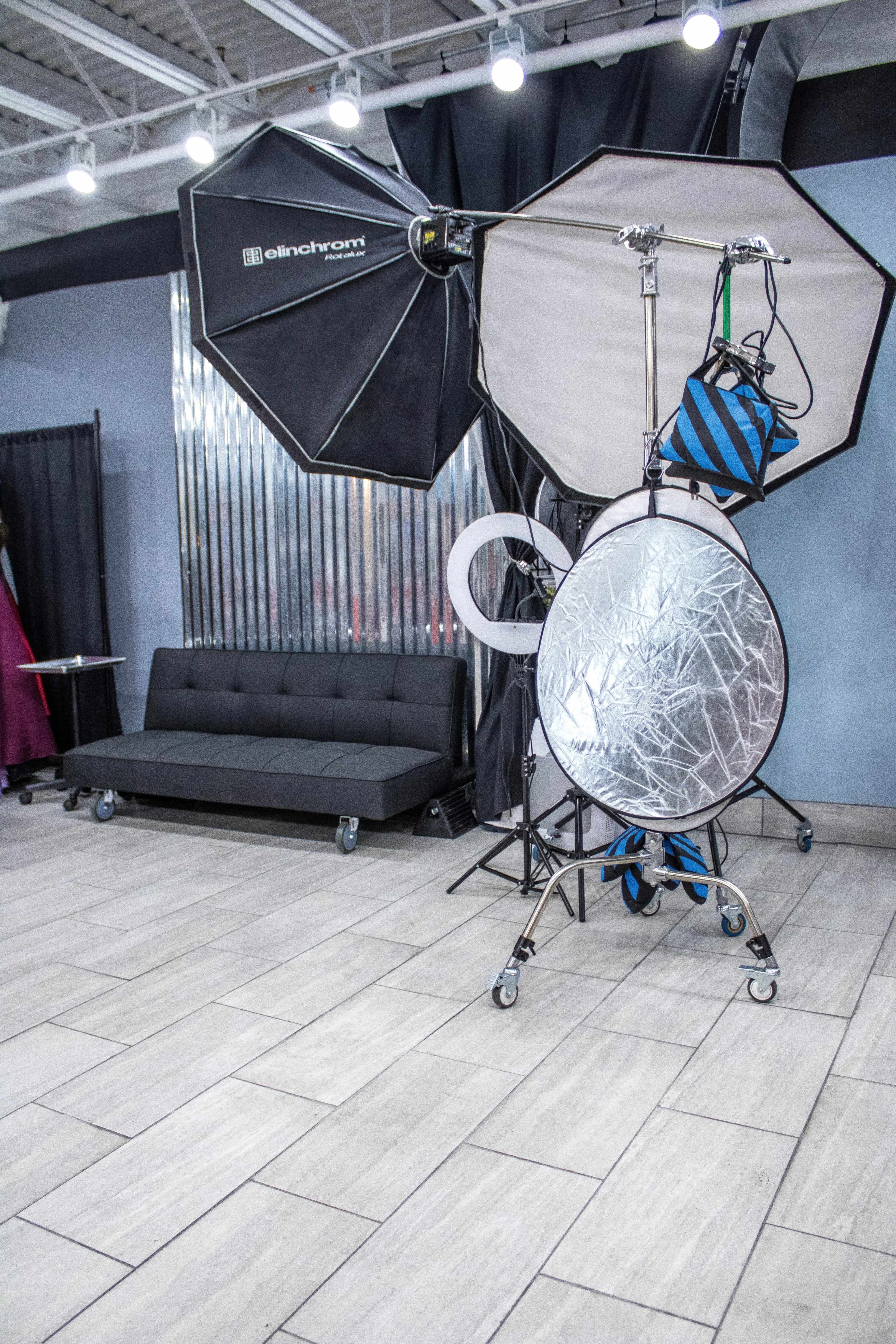 A photography setup features large softbox lights and a reflective disc next to a black sofa in a studio.