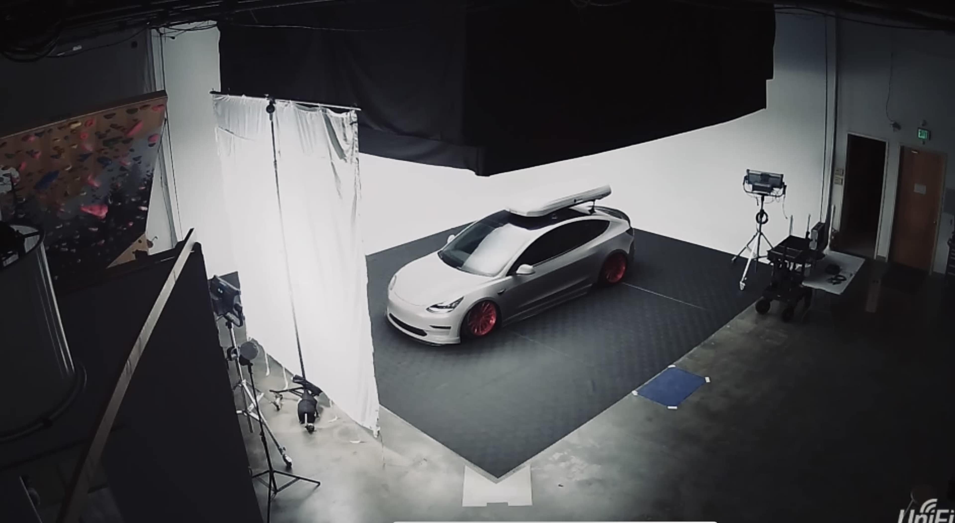 A car on a staged set with lighting equipment and a backdrop in a photography studio.