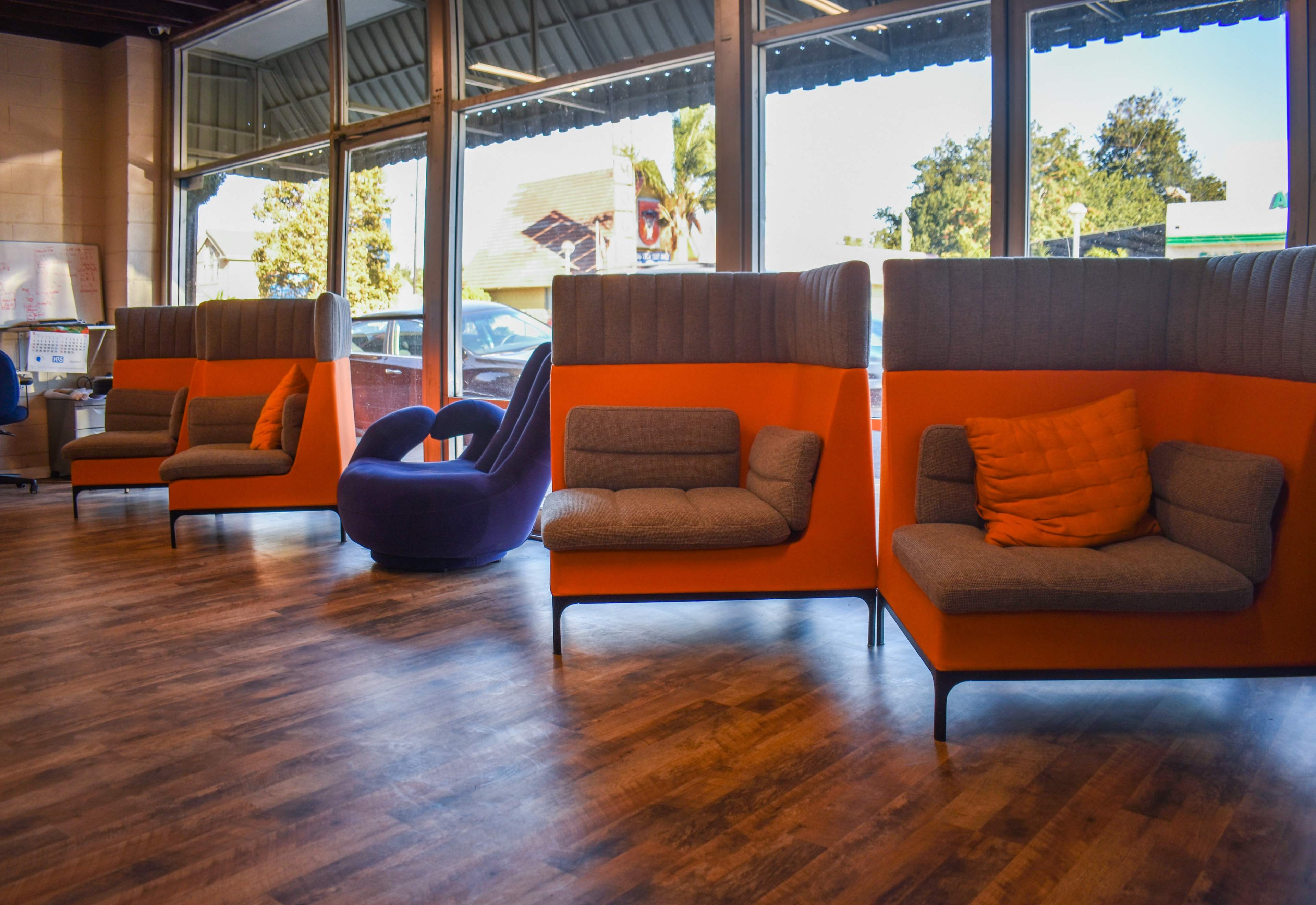 A modern interior featuring two pairs of orange and gray lounge chairs and a purple seating area with large windows allowing natural light to enter.