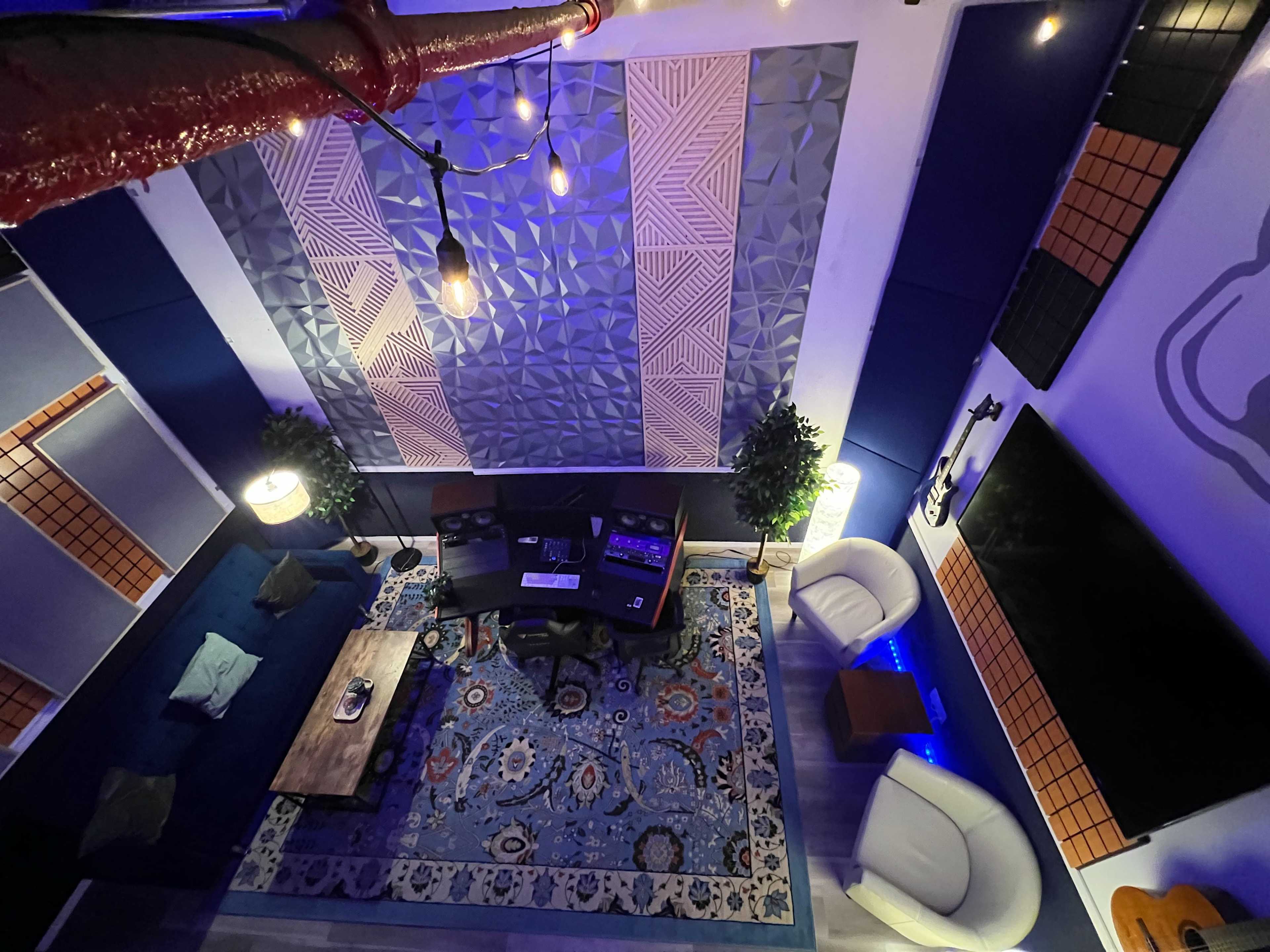 A modern room with a patterned rug, a coffee table, two chairs, studio monitors, and acoustic panels on the walls.