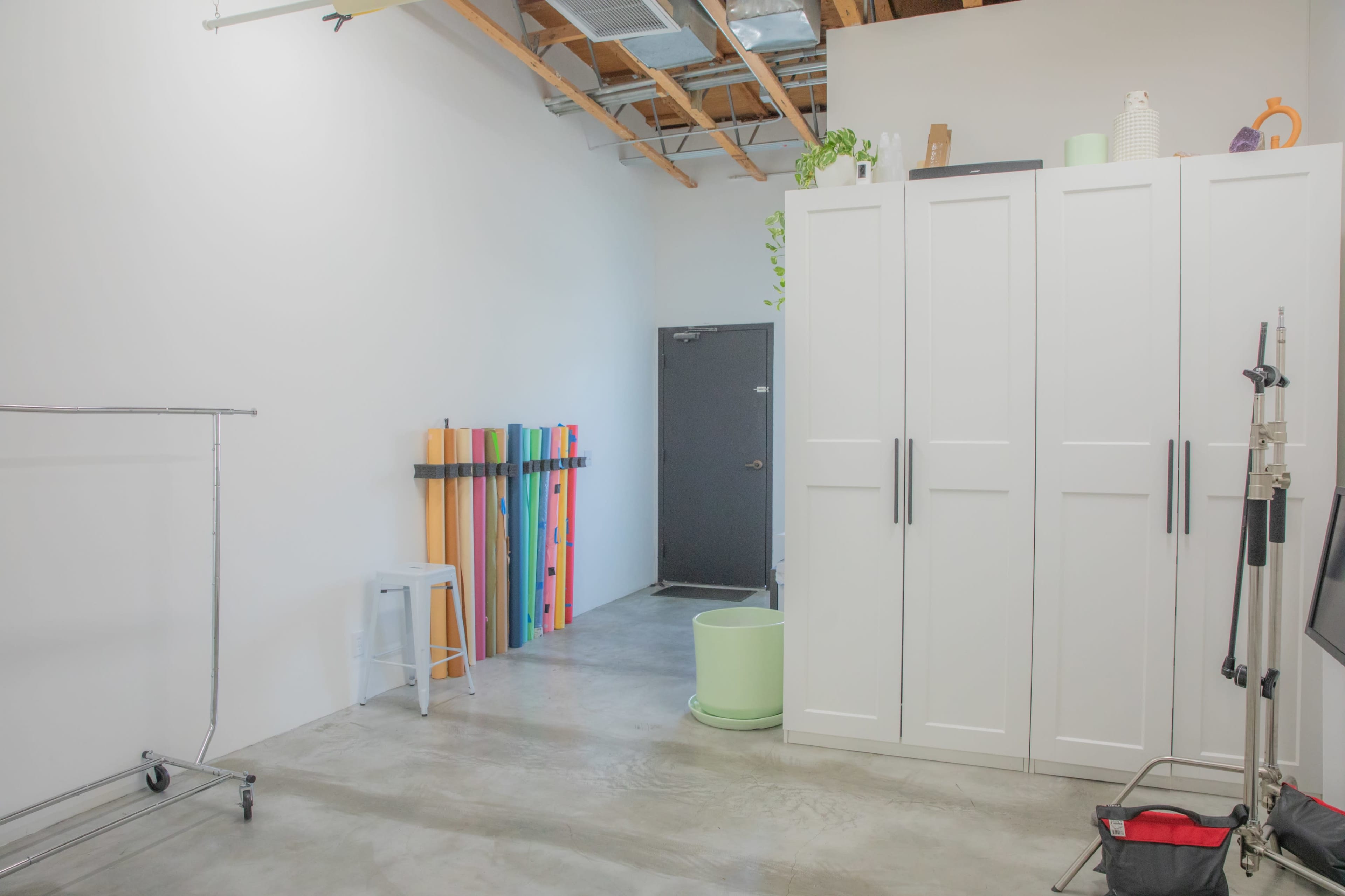 A spacious interior with a white wall, a dark door, a storage cabinet, colorful vertical strips against the wall, and a green container on the floor.