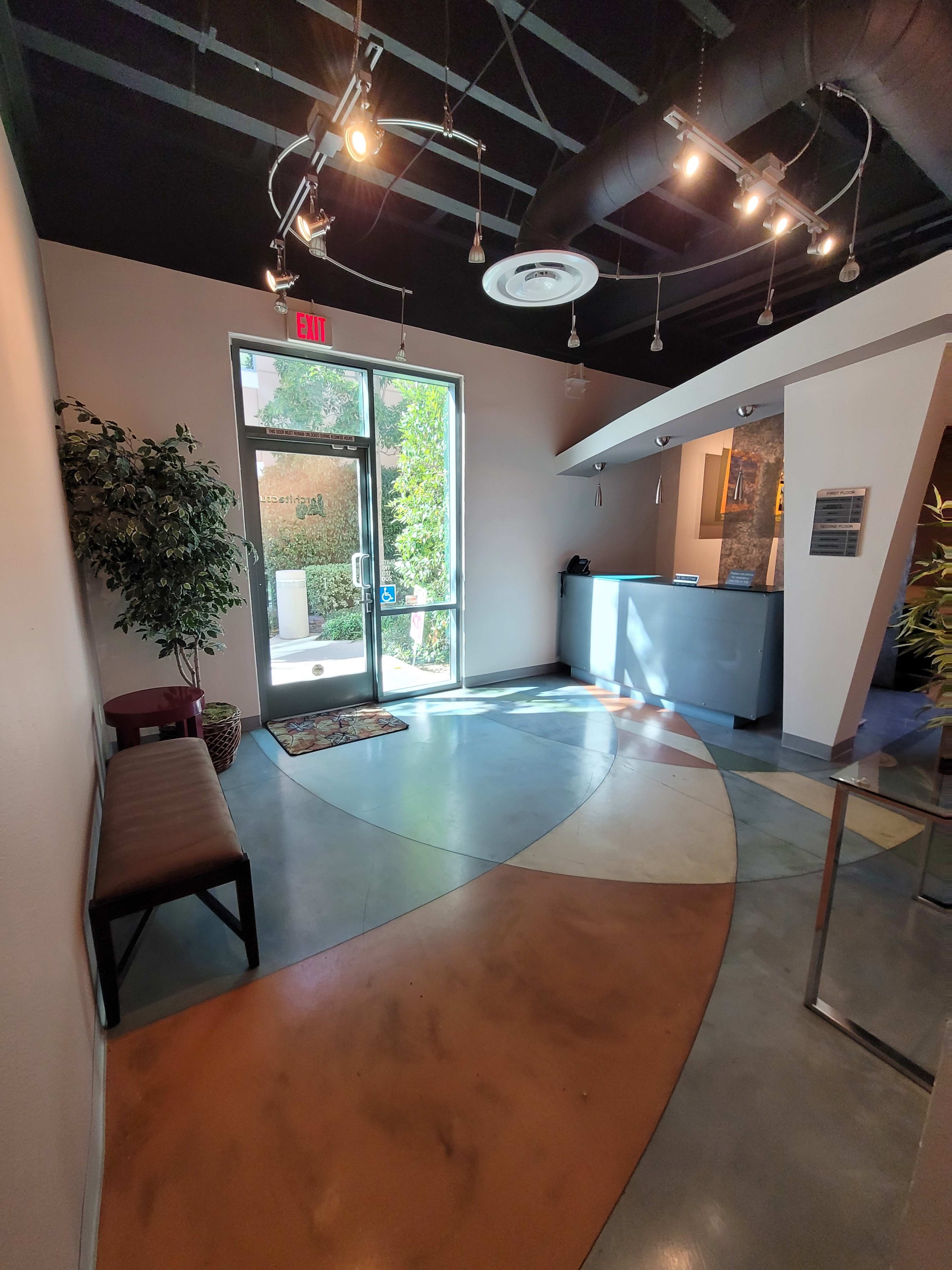 A modern reception area with a front desk, a bench, and large windows allowing natural light to enter.