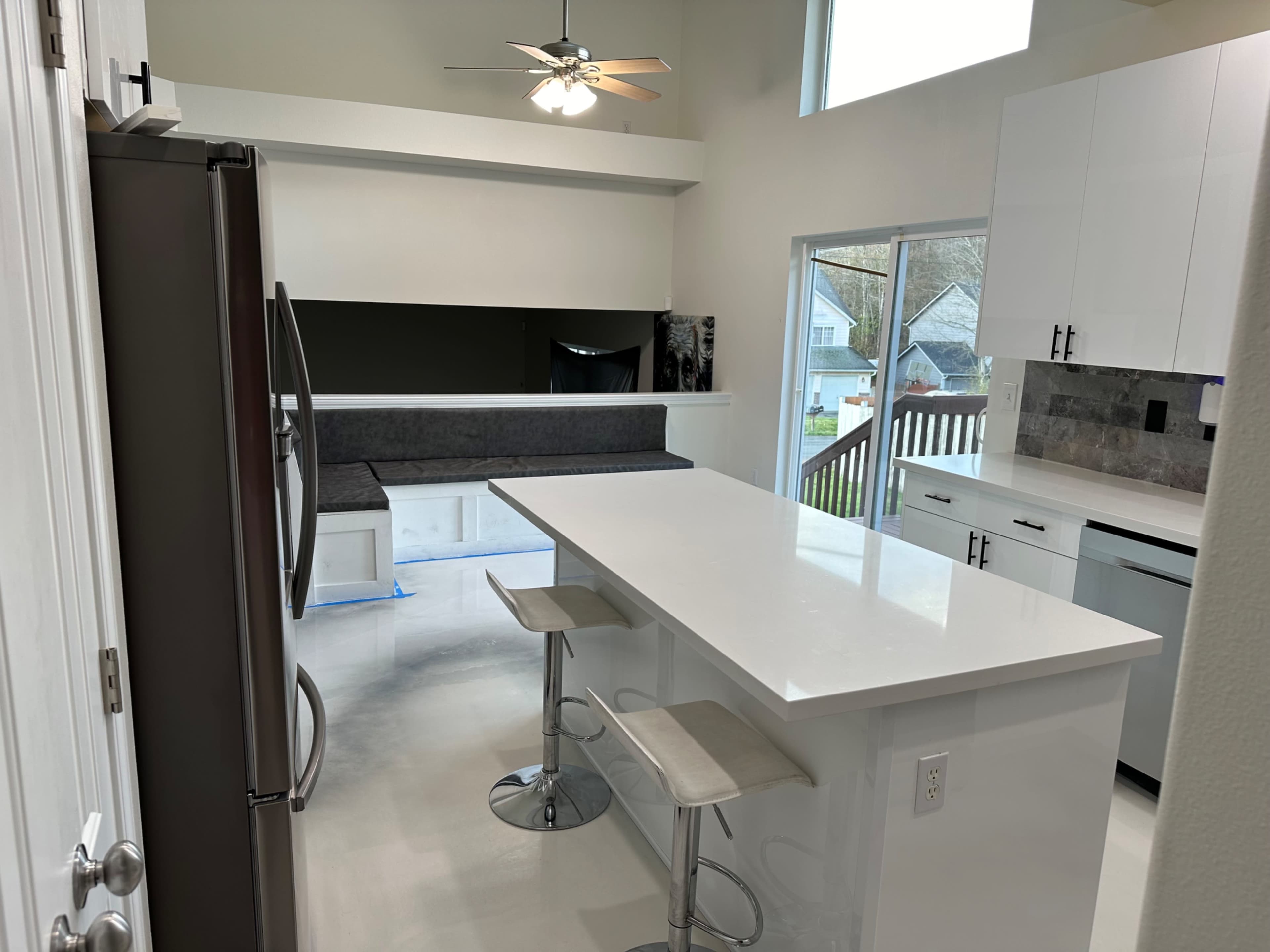 The kitchen features white cabinets, a large island with bar stools, and a built-in seating area beside a window.