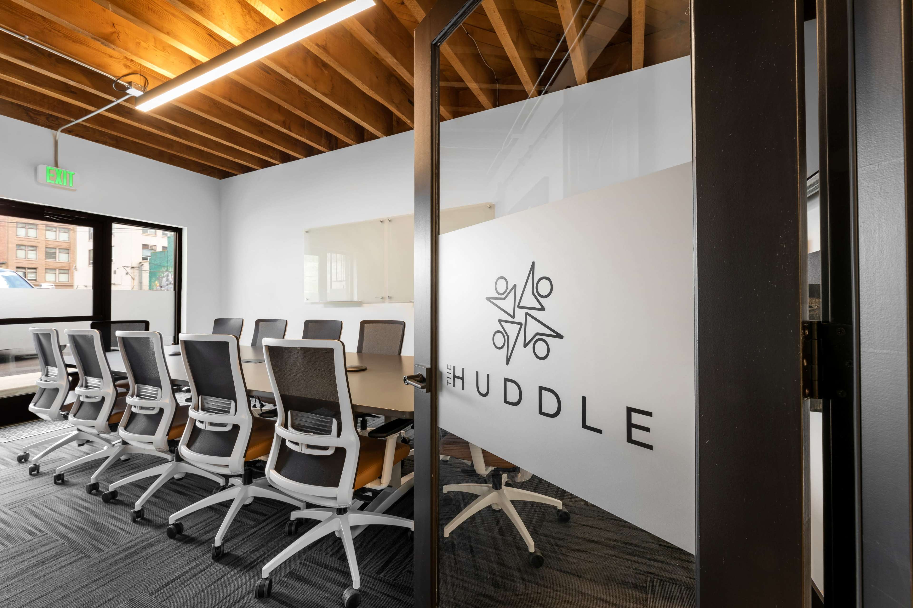 A conference room with a large table and multiple office chairs is depicted, featuring glass doors with the word "HUDDLE" prominently displayed.
