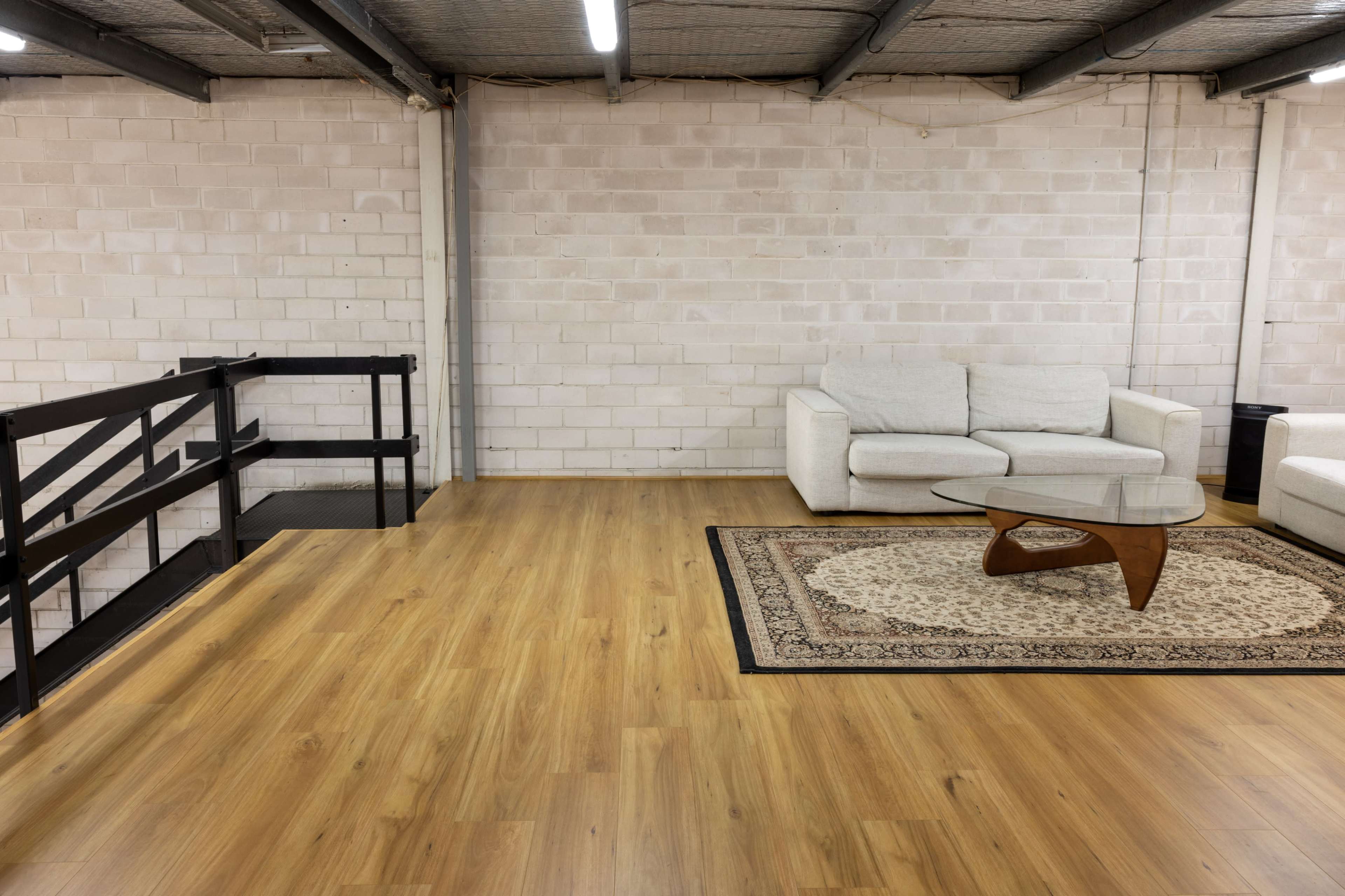 A spacious, minimally furnished room with a couch, a coffee table on a patterned rug, and a railing leading to a lower level.