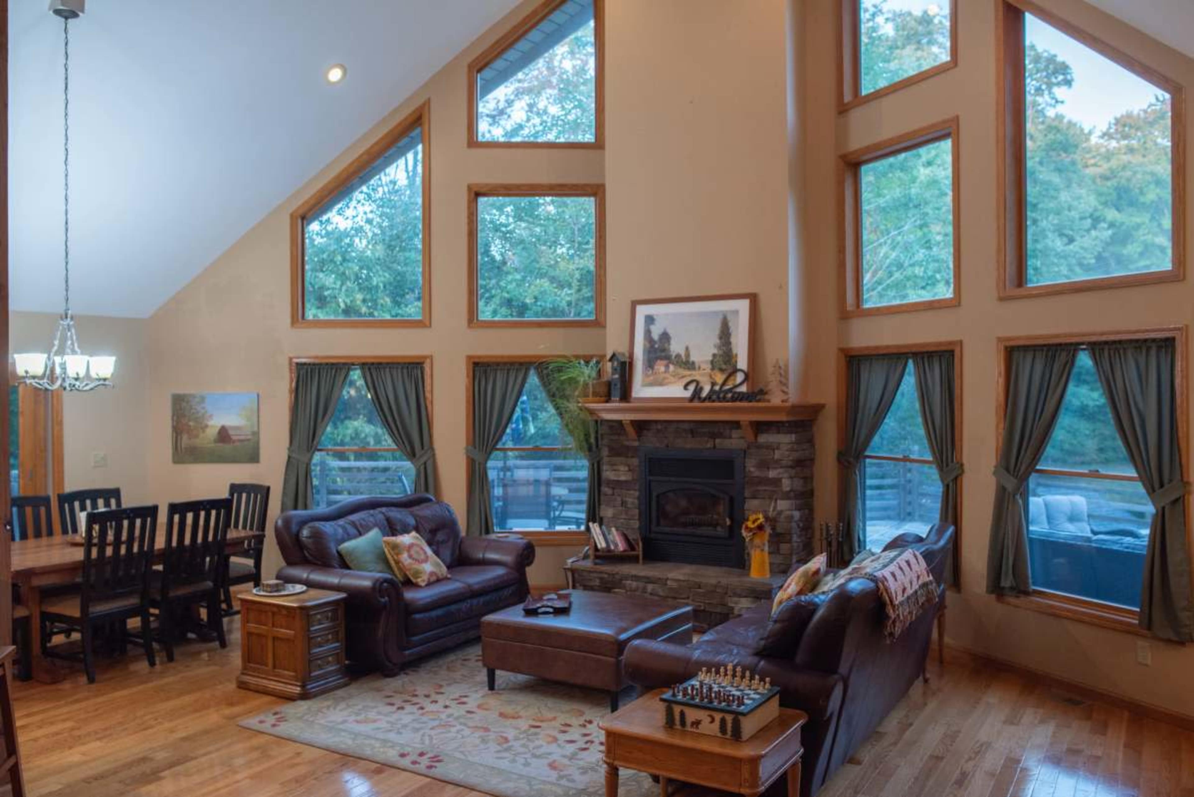 The living room features large windows, a stone fireplace, and a mix of seating and dining areas.