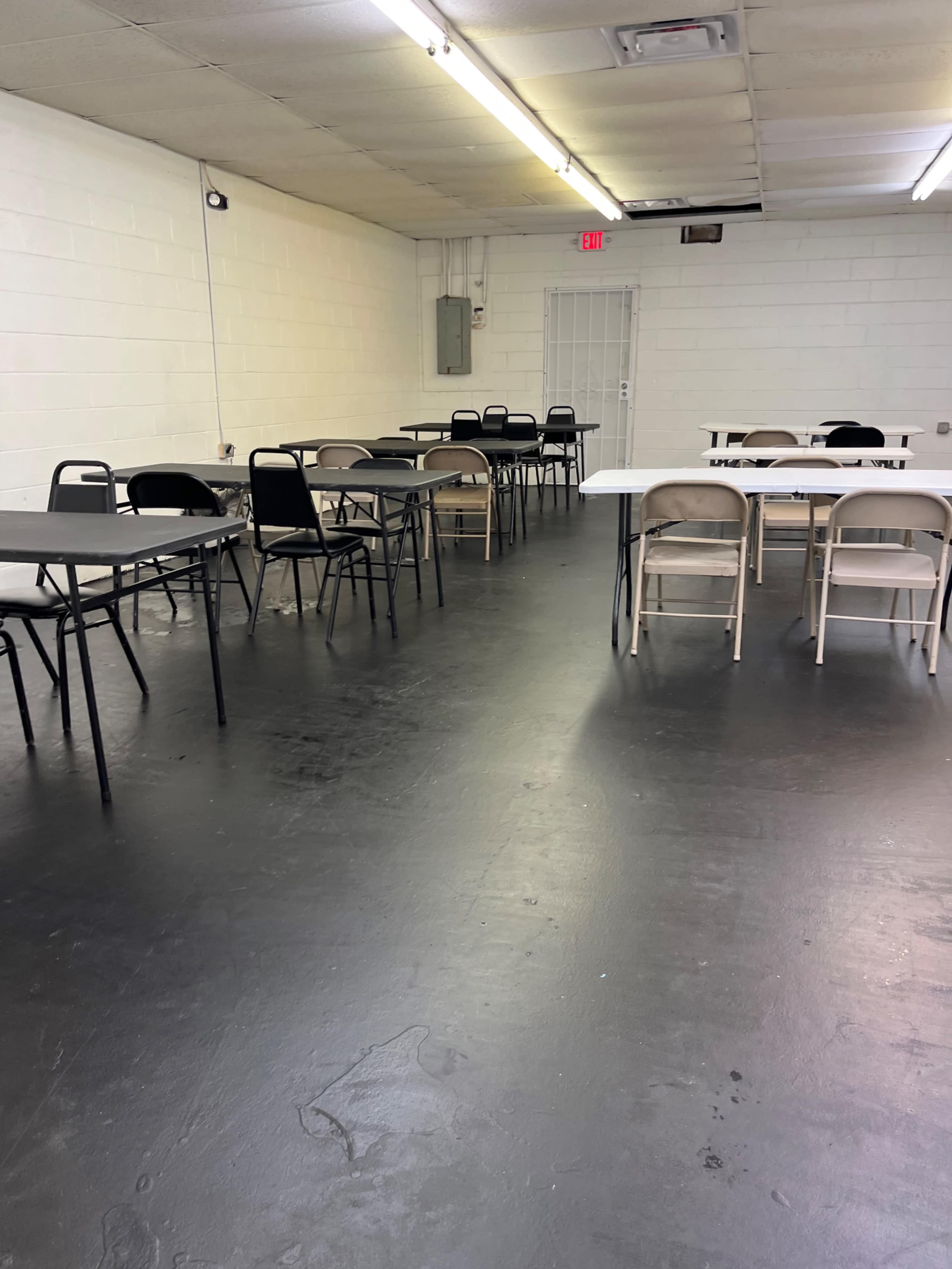 A spacious, empty room with several tables and chairs arranged around the space.