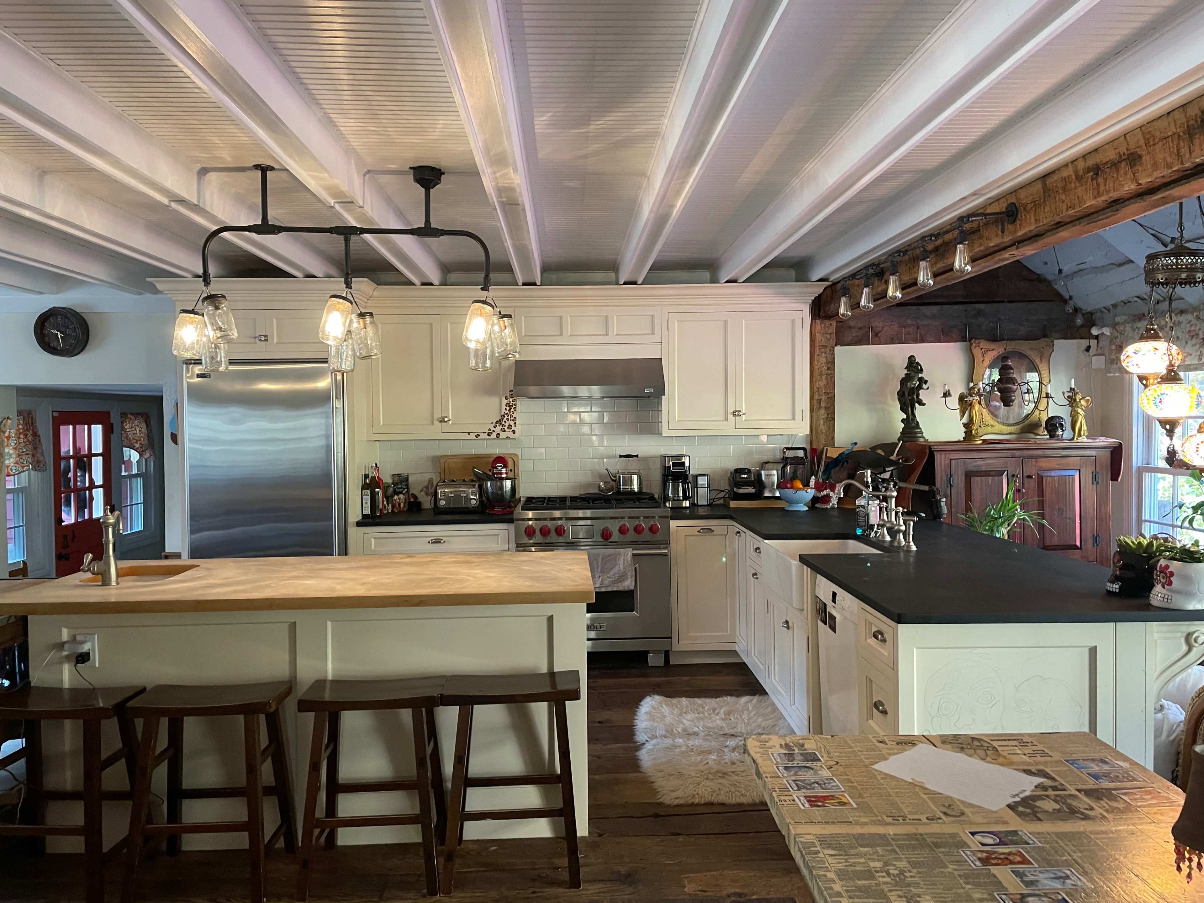 A spacious kitchen featuring a central island with bar stools, stainless steel appliances, white cabinetry, and wooden beams across the ceiling.