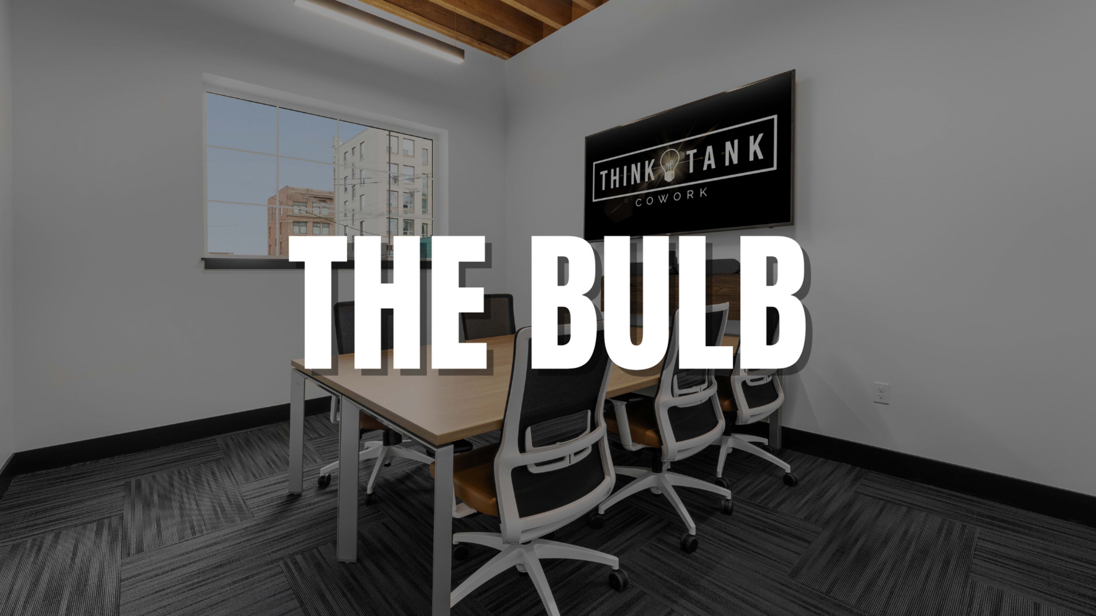 A contemporary conference room in a coworking space with a large window and a table surrounded by several chairs.