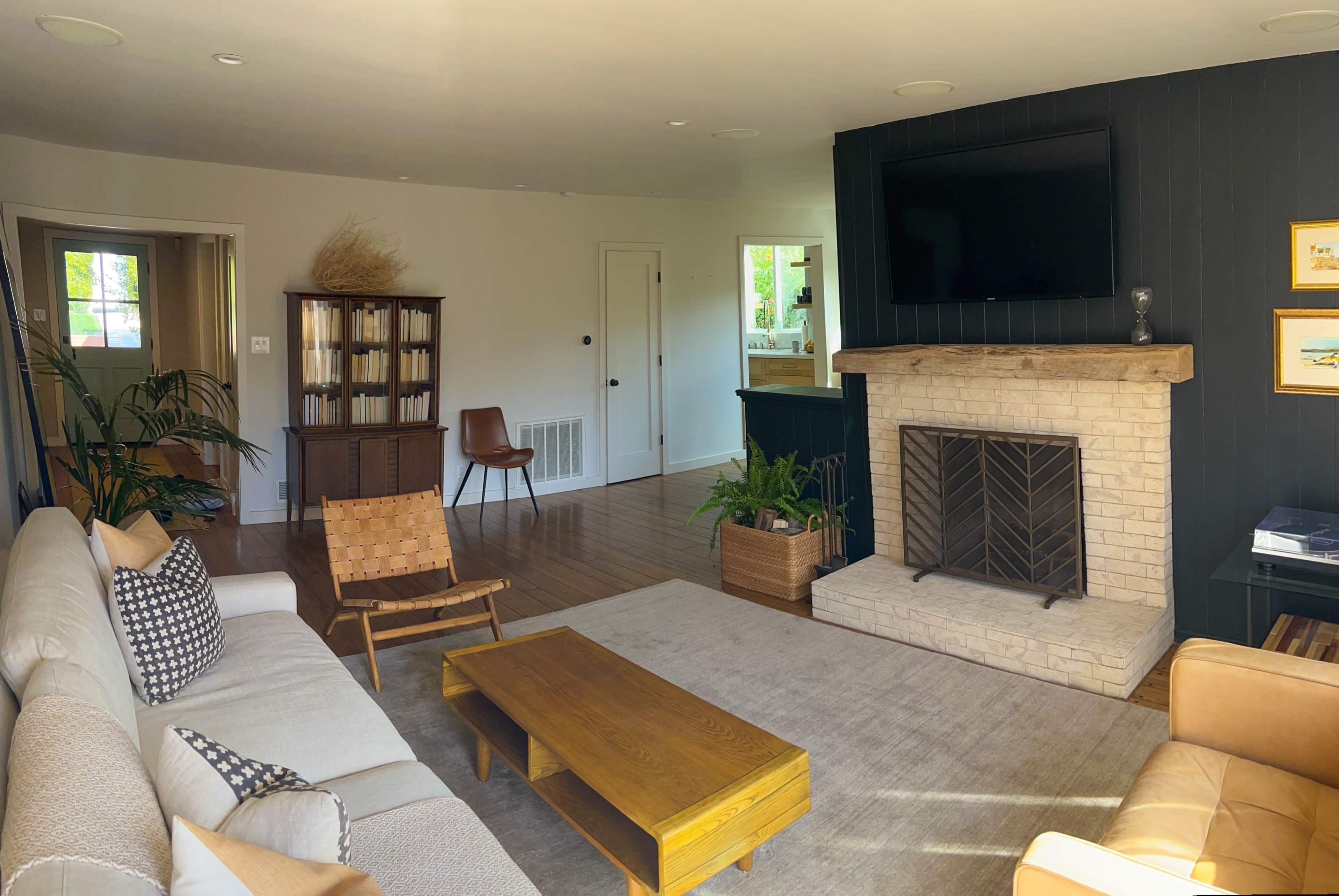A modern living room with a fireplace, a large window, and a sectional sofa arranged around a wooden coffee table.