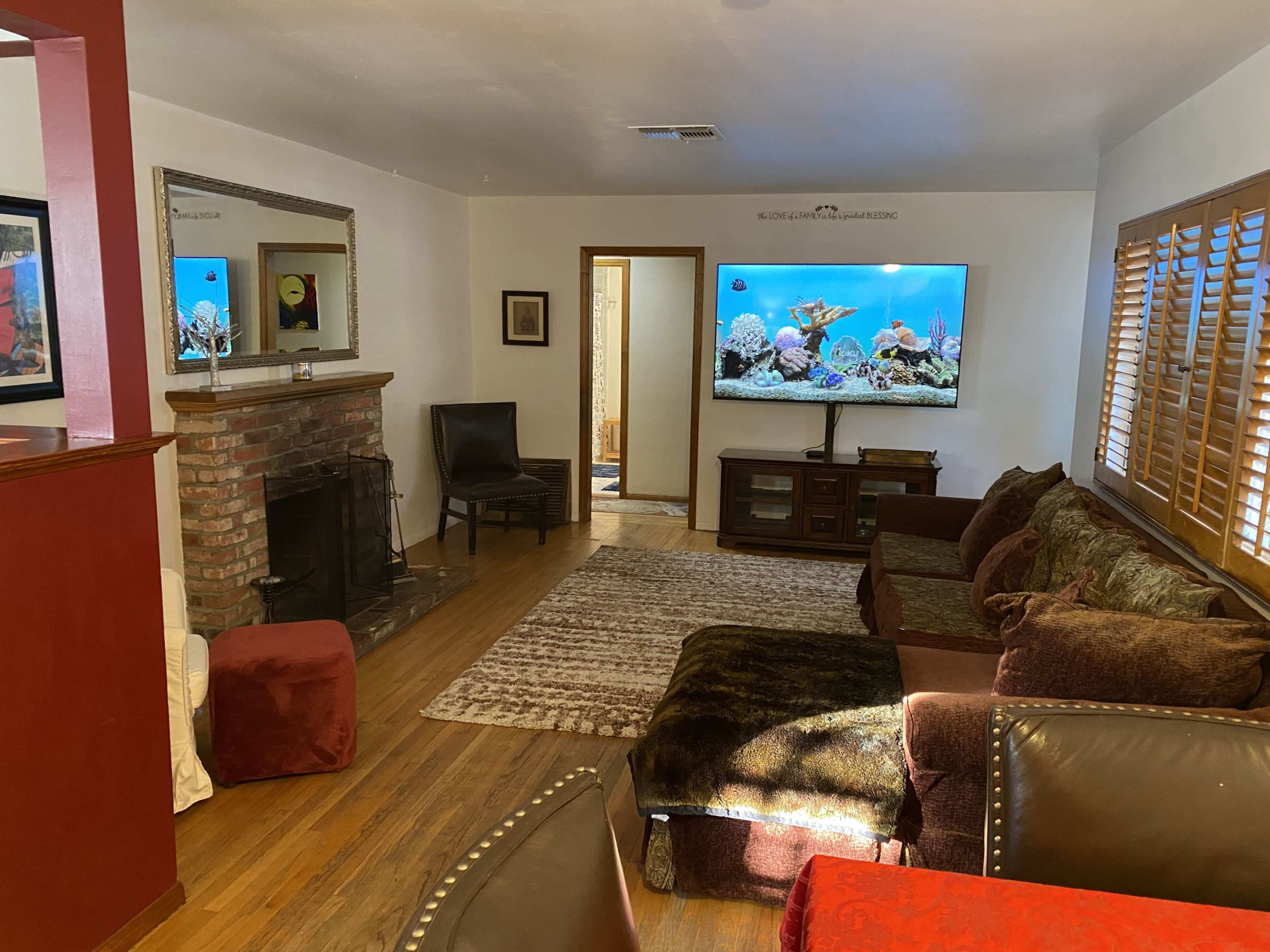 The living room features a sectional sofa, a brick fireplace, and a large television displaying an aquarium scene.