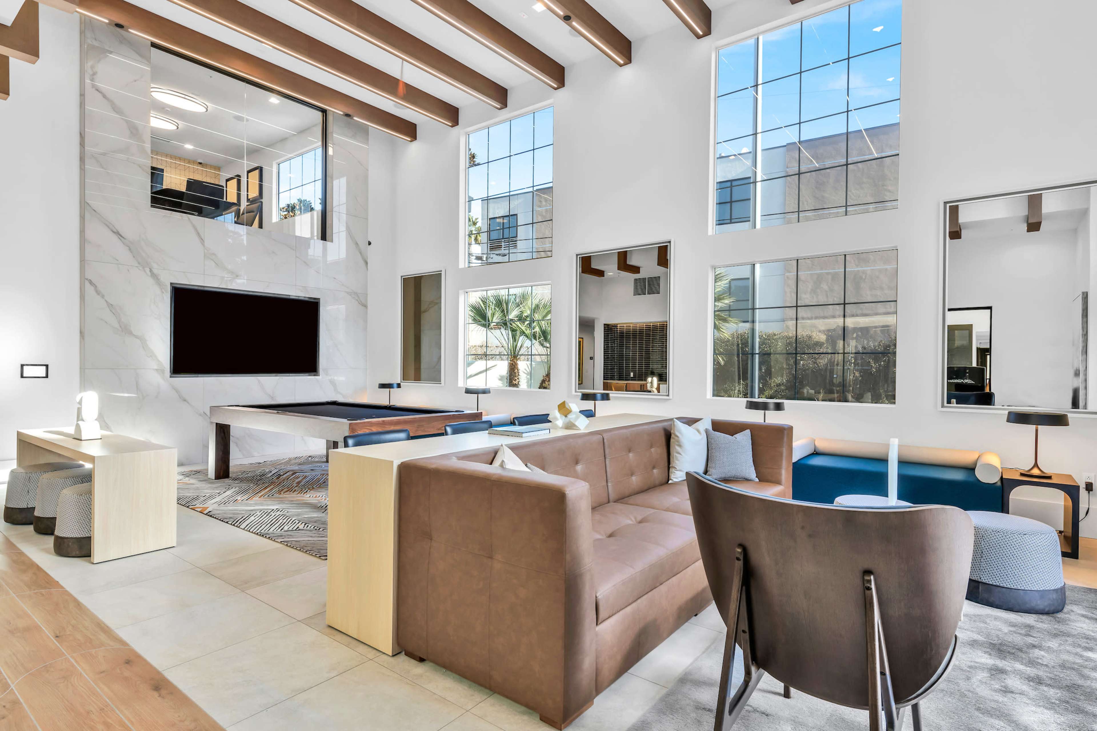 The spacious living room features large windows, a marble accent wall with a television, and modern furniture arranged around a coffee table.