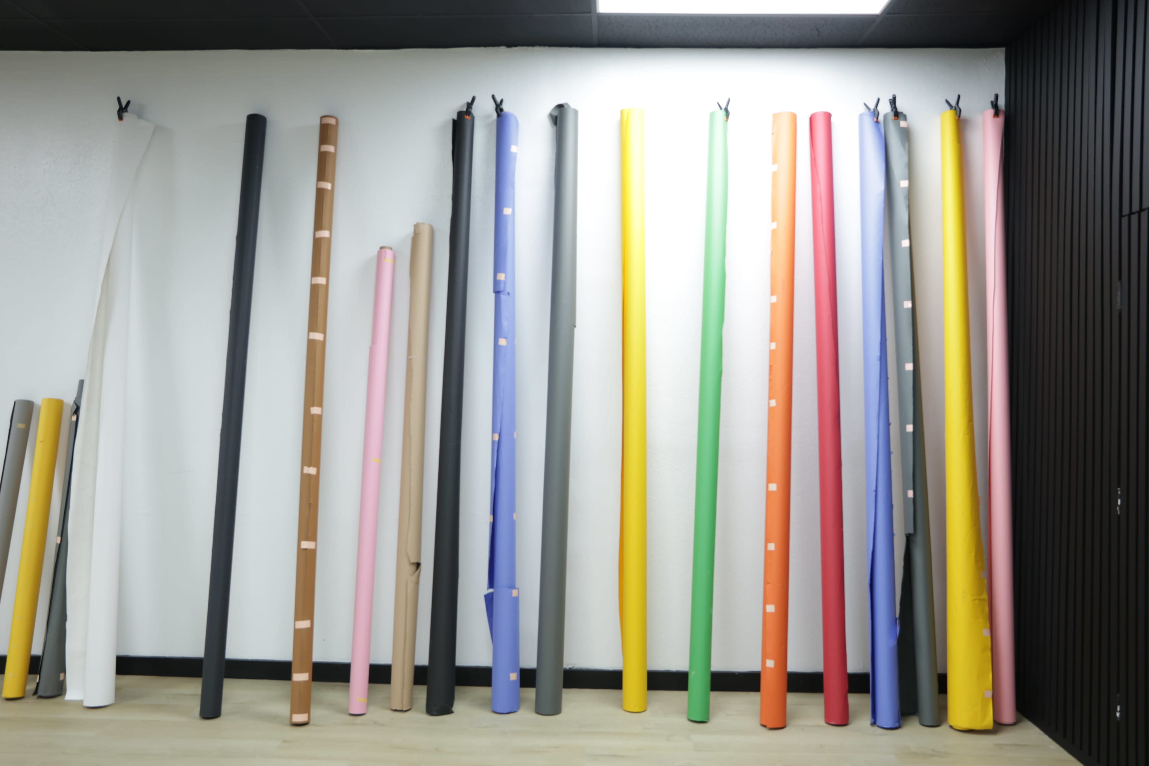 A collection of rolled paper sheets in various colors stands arranged vertically against a white wall.