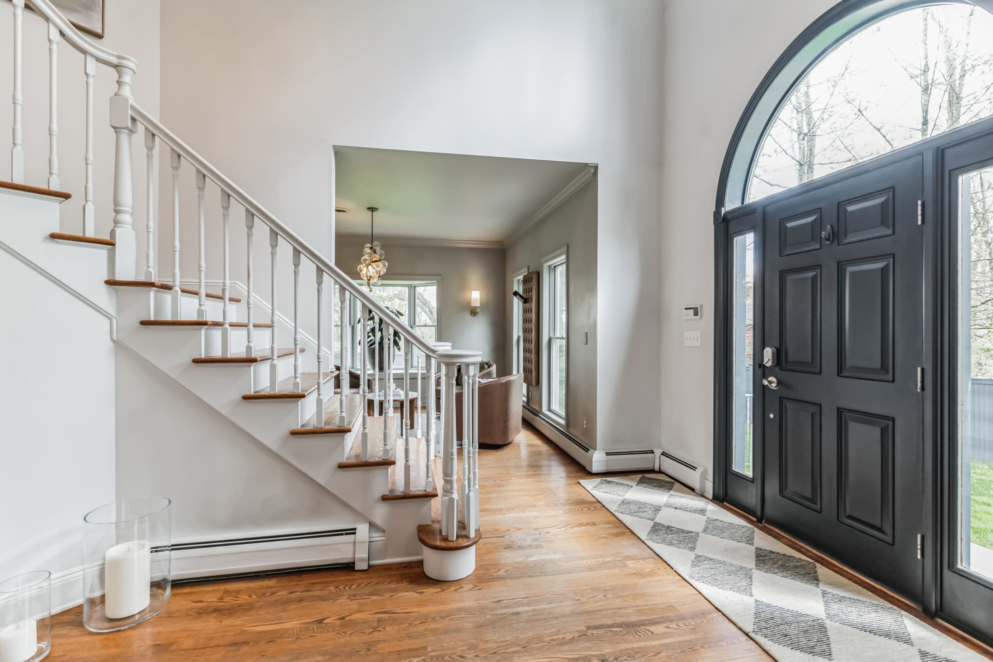 A bright entryway featuring a staircase with wooden steps, a decorative chandelier, and a large arched doorway with a black front door.