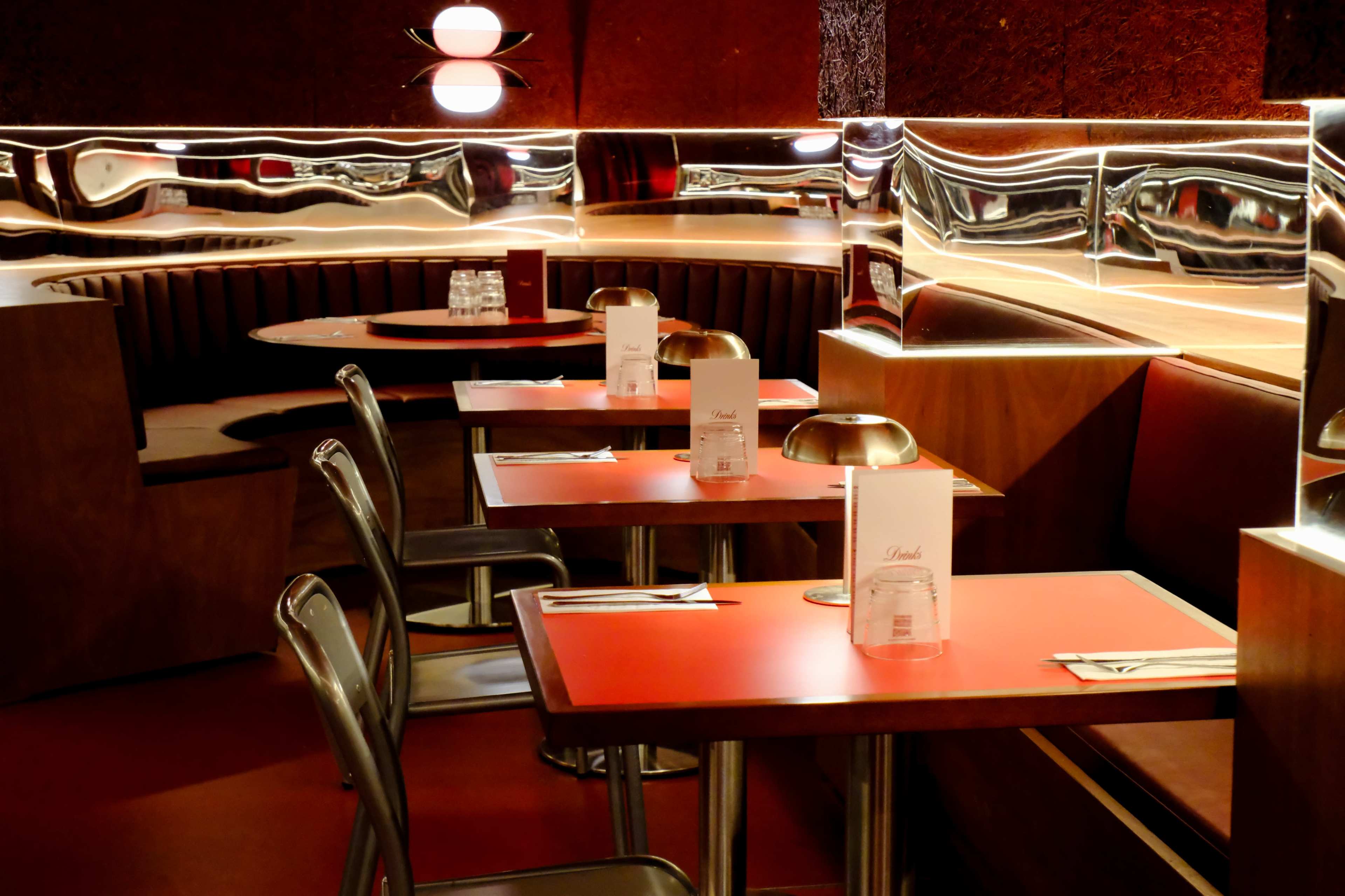 The image depicts a modern restaurant interior with sleek red tables, metallic accents, and curved seating areas.