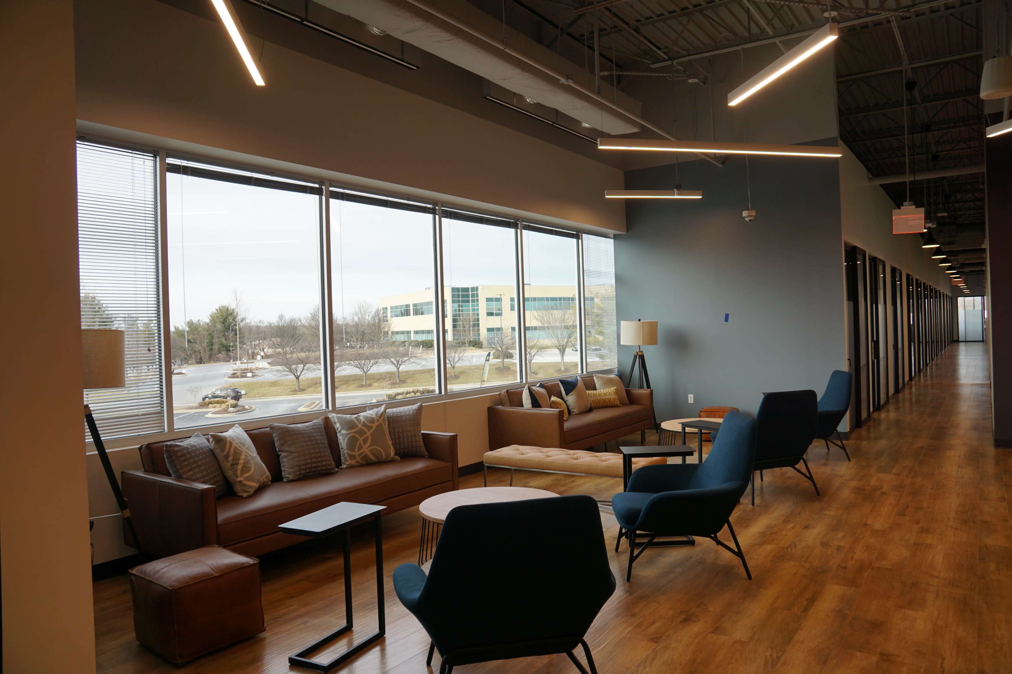 A modern office lounge area with large windows, comfortable seating, and a wooden floor.