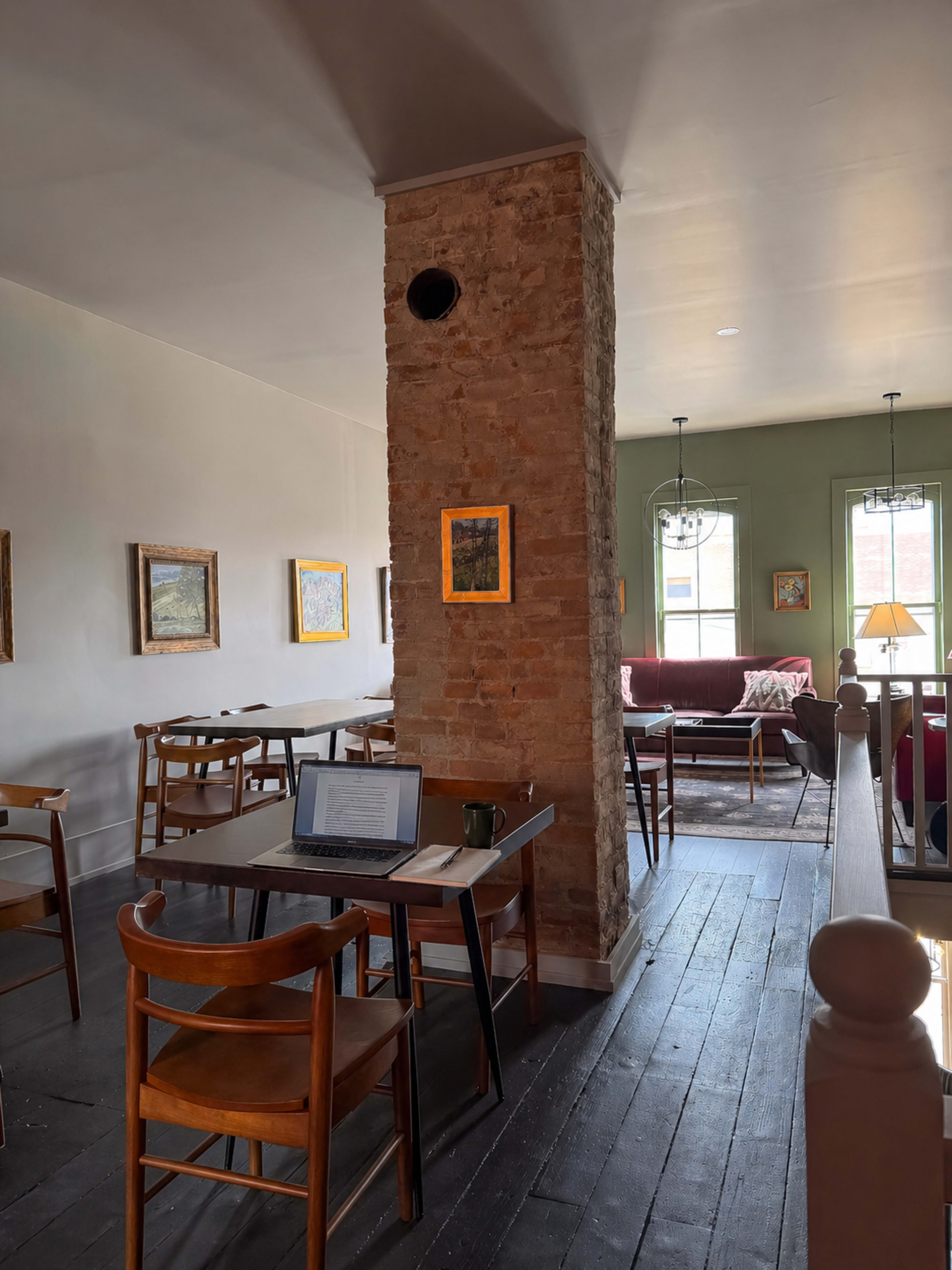 The image shows a cozy café with wooden furniture, a stone column, and art on the walls, featuring a laptop on one of the tables.