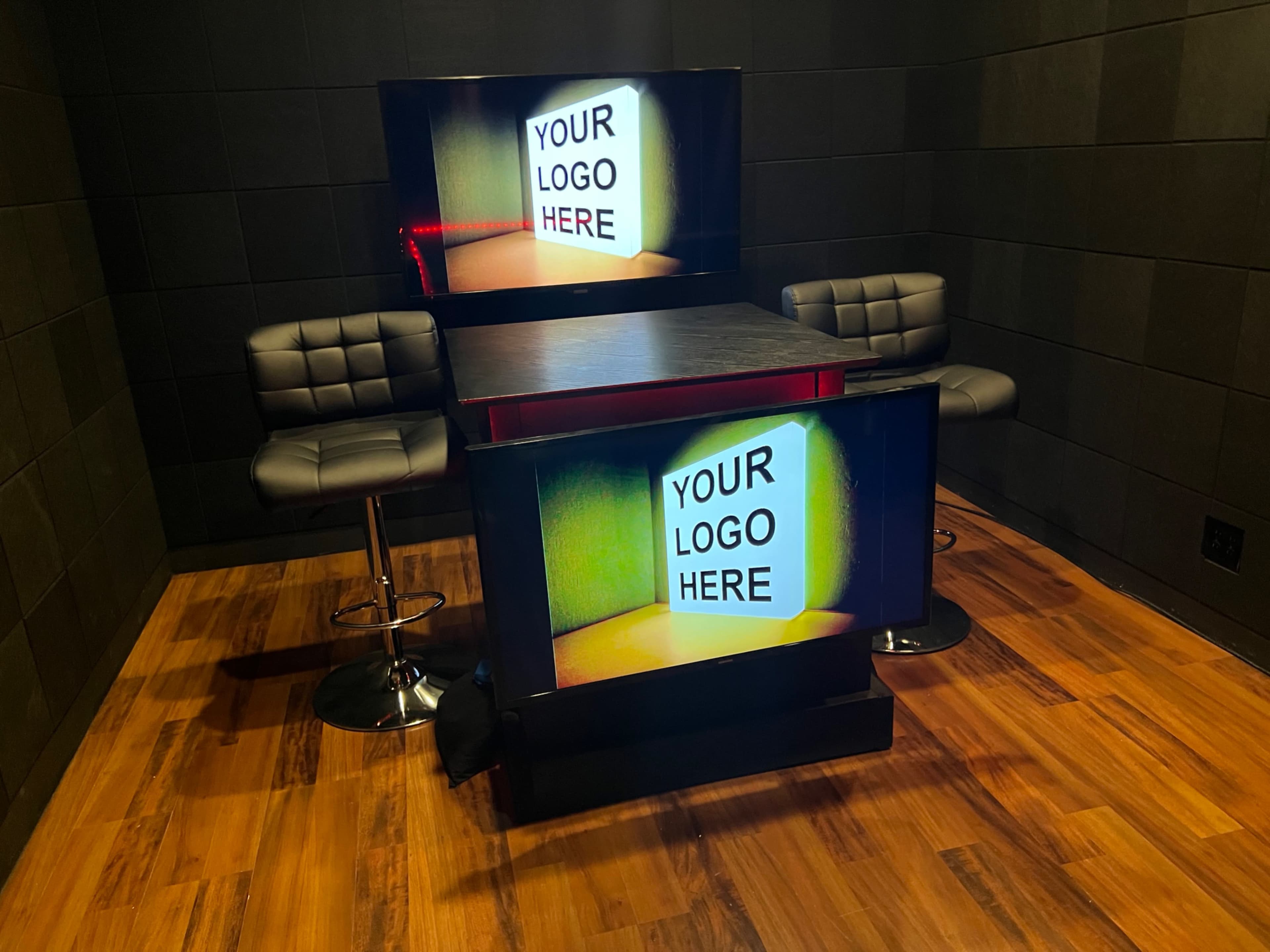 A modern setup featuring two screens and a table with two black bar stools in a dark room.
