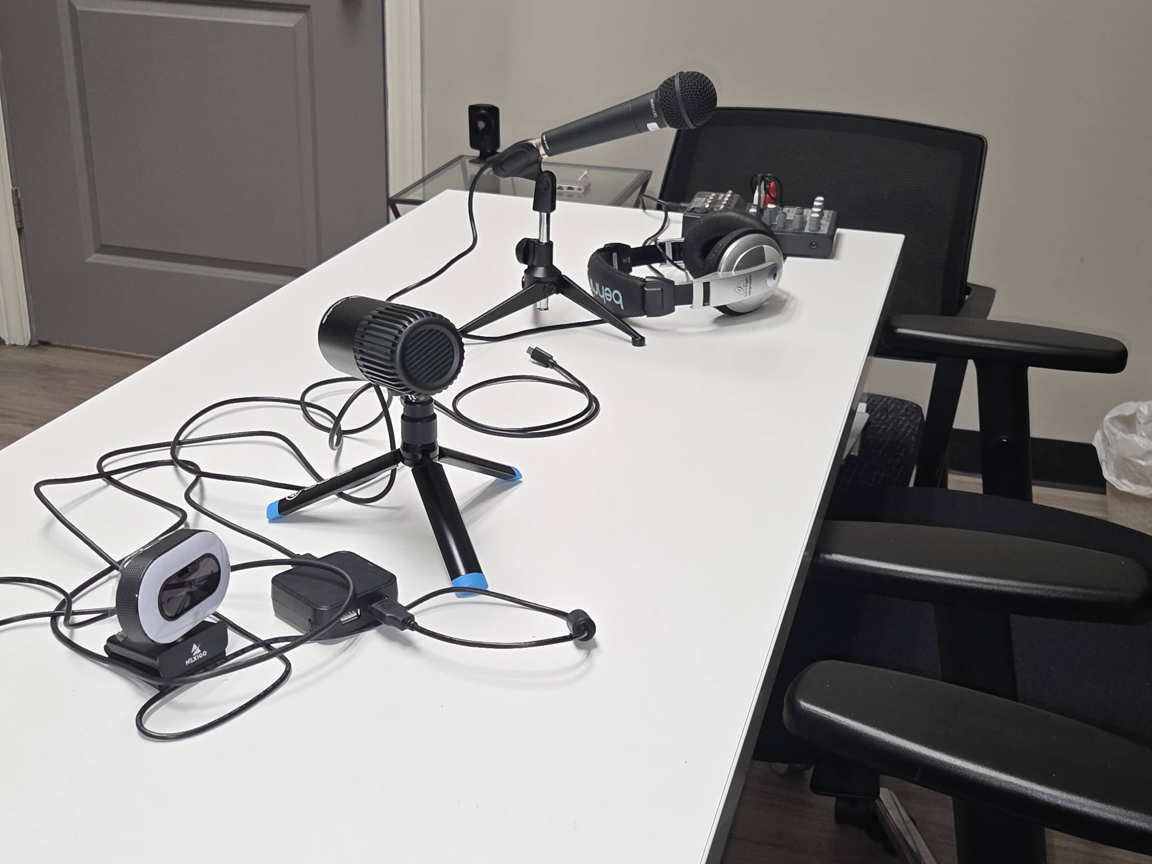 A white table is set up with two microphones, a pair of headphones, and various audio equipment, all connected by cables.