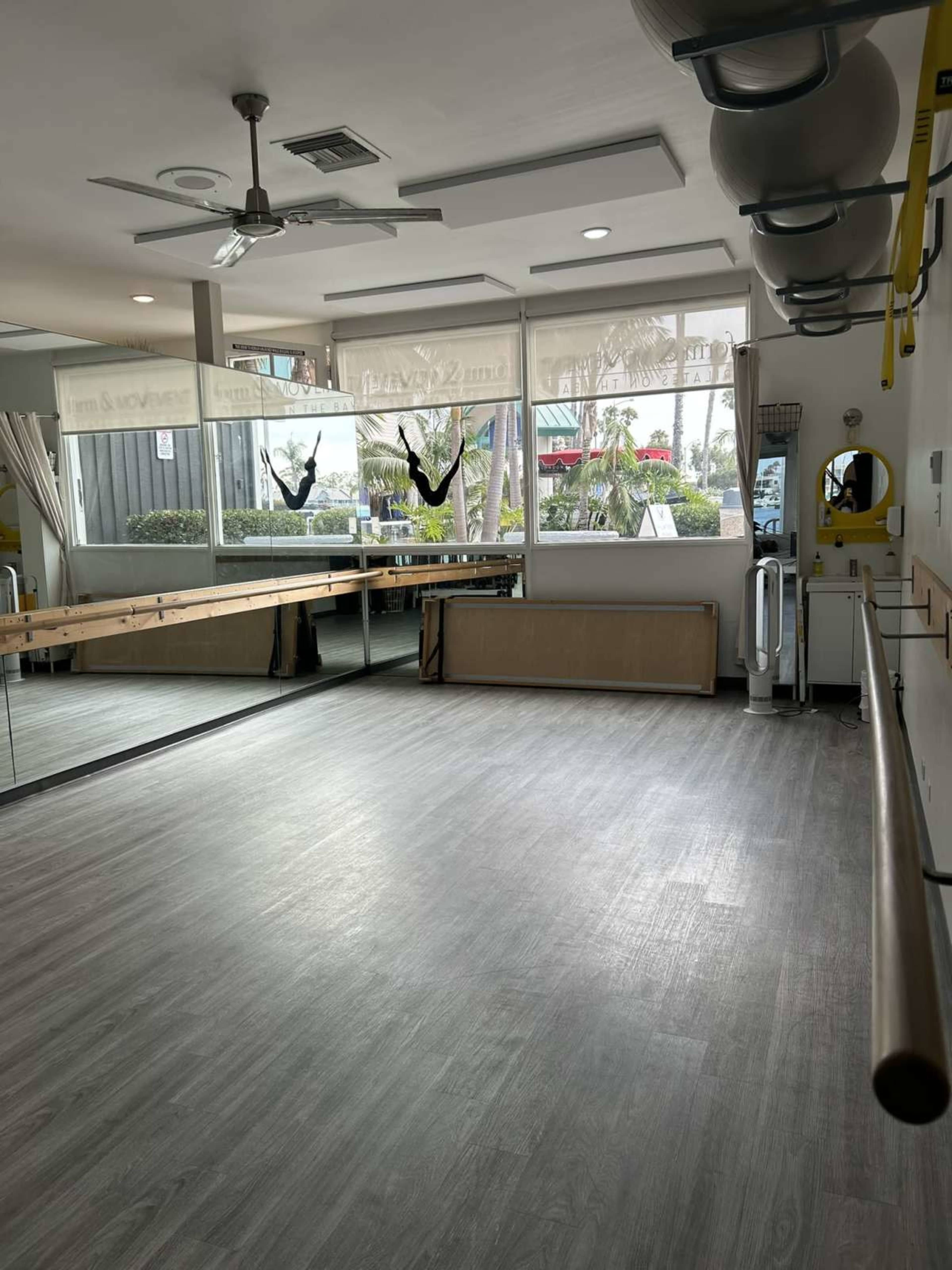 The image shows a bright, empty exercise studio with large windows overlooking greenery and a mirrored wall.
