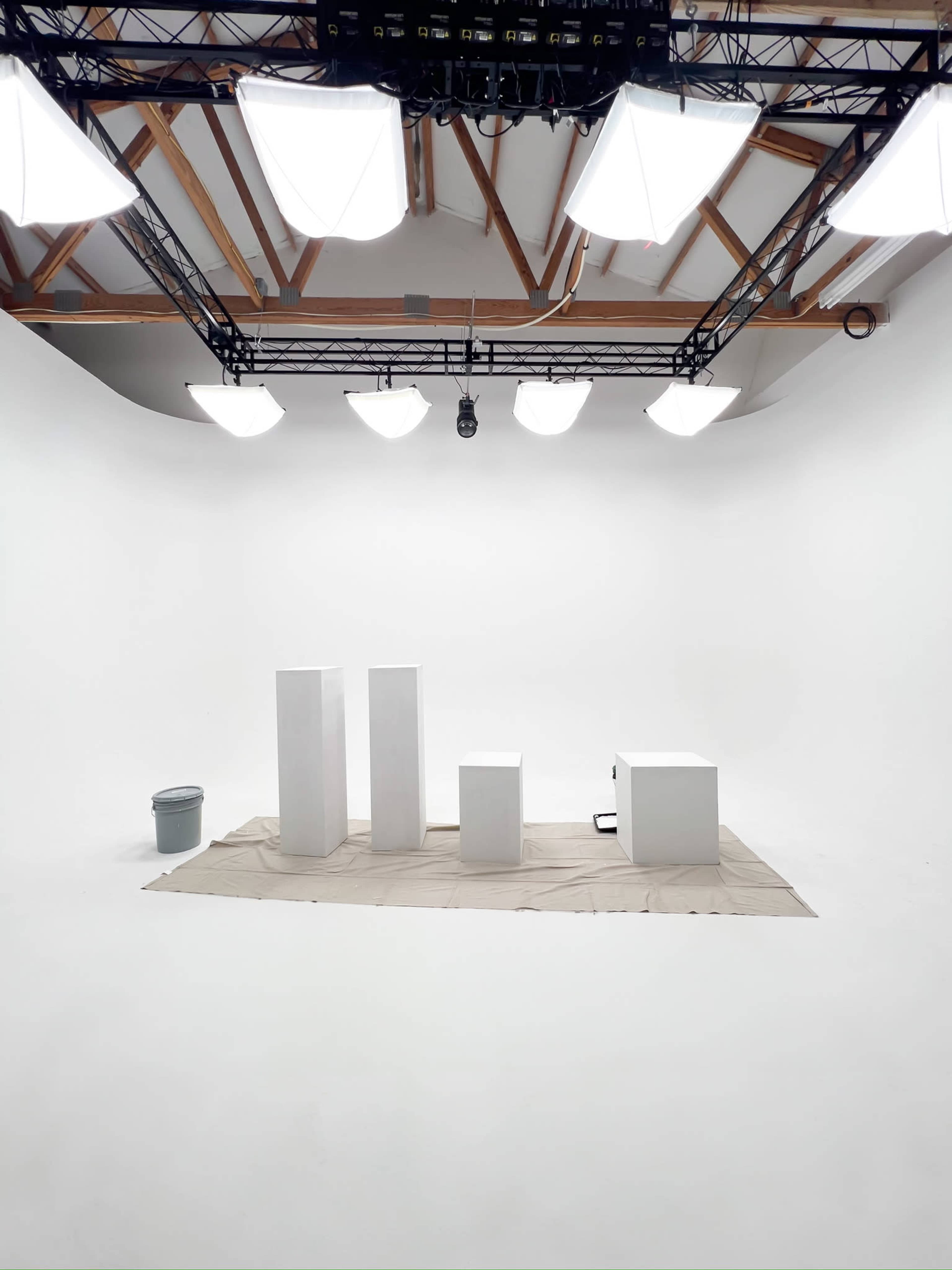 A photography studio with a series of white display platforms positioned on a beige cloth, surrounded by several ceiling lights.