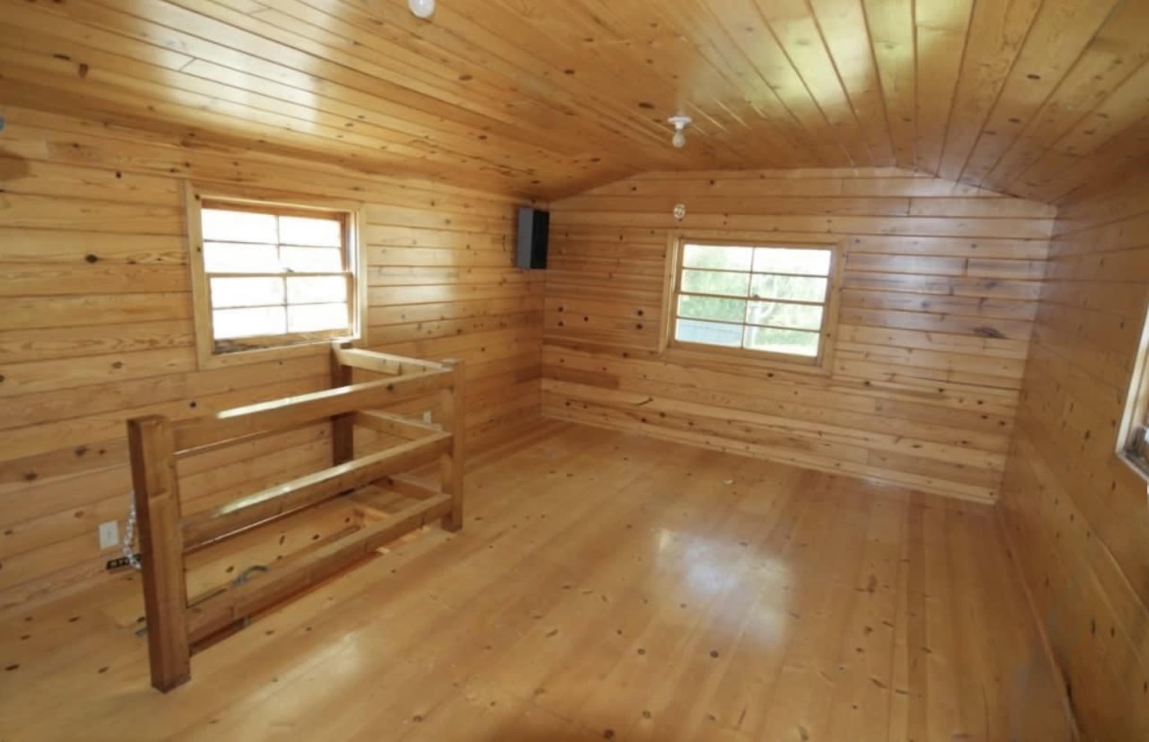 A wooden room with walls, ceiling, and floor made of polished pine wood, featuring two windows and a railing on one side.