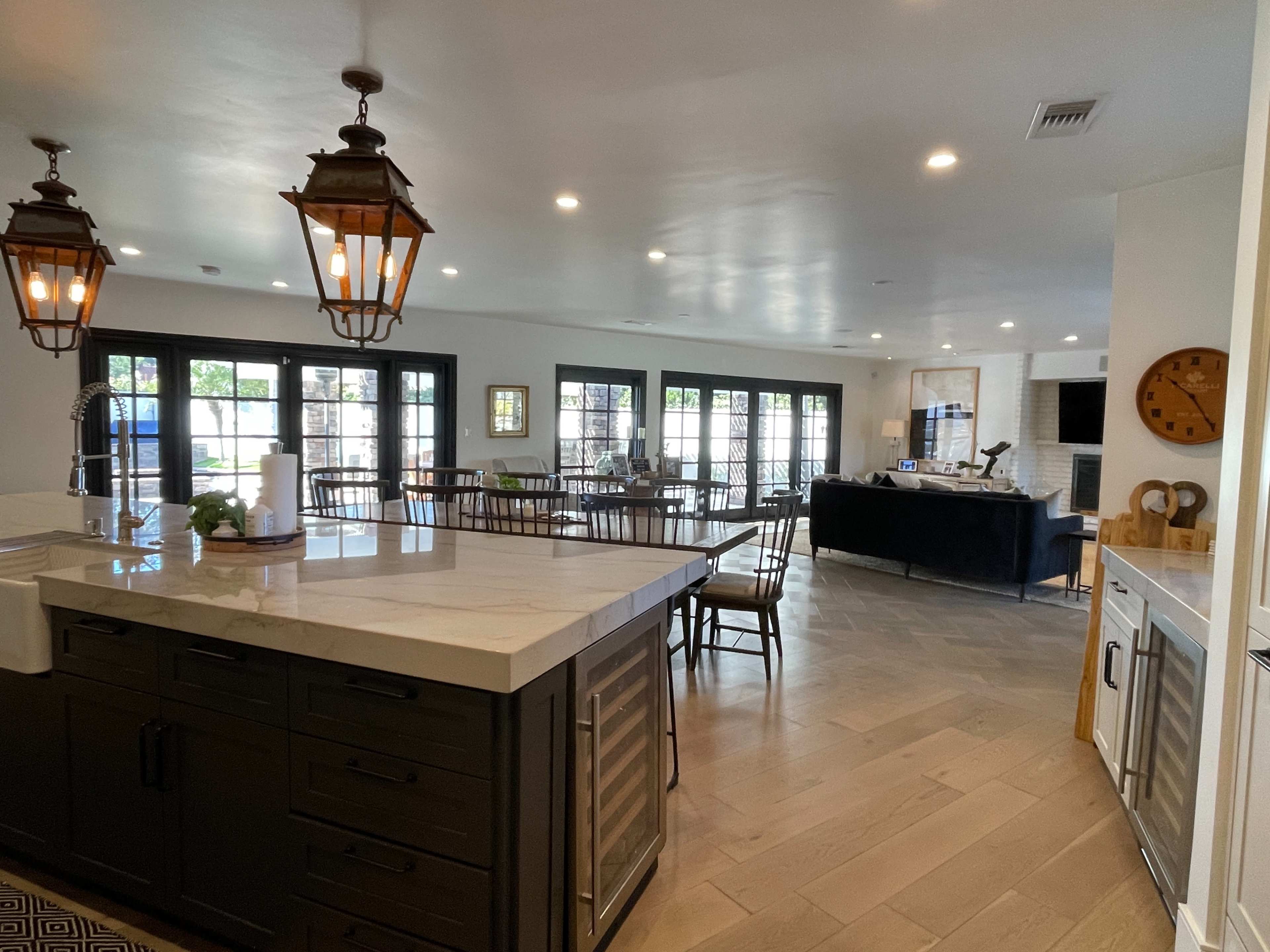 A spacious kitchen and dining area with a large island, wooden tables, and a living room visible in the background.