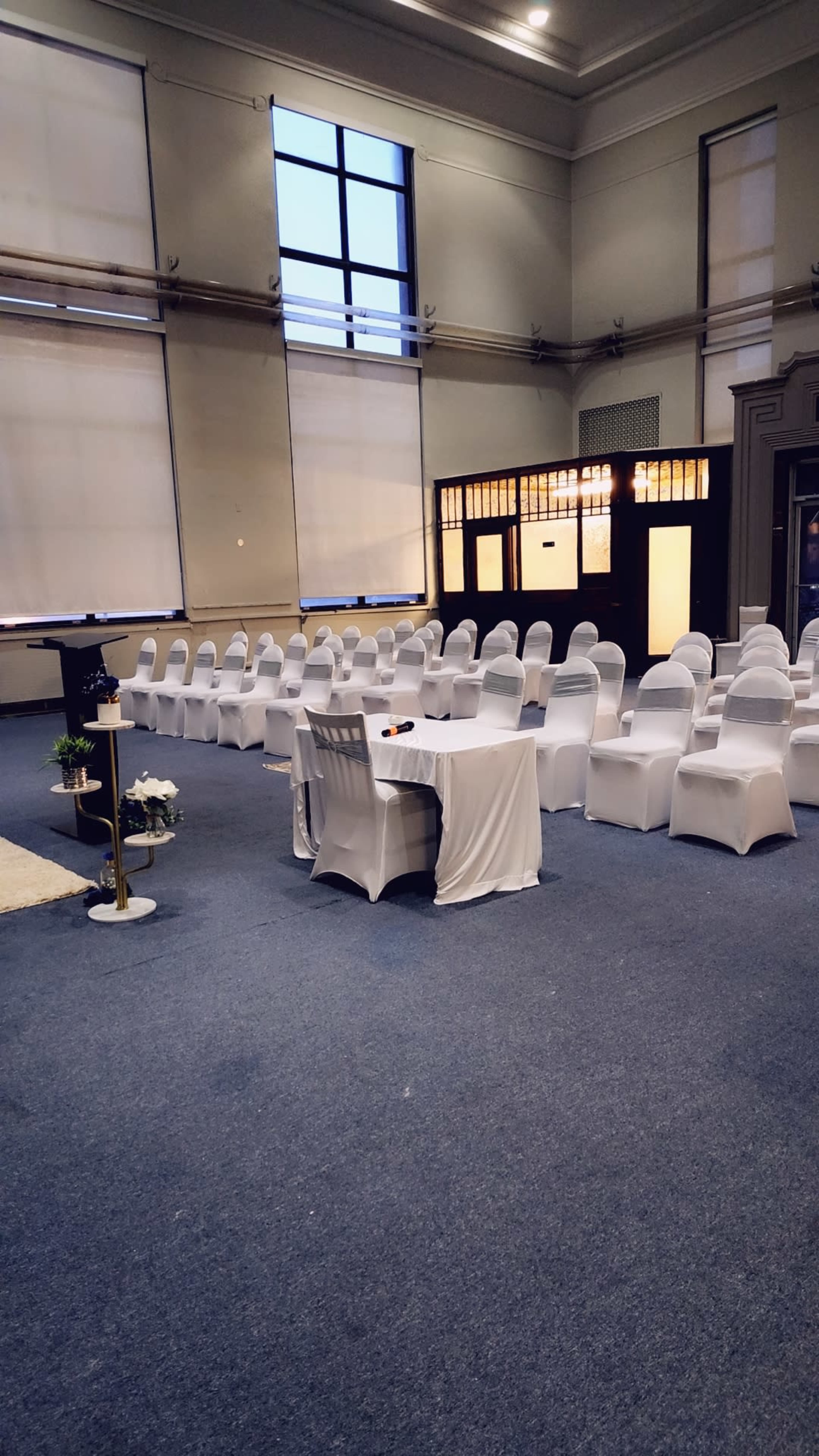 A formal setting with rows of white-covered chairs facing a small table in a spacious, well-lit room.