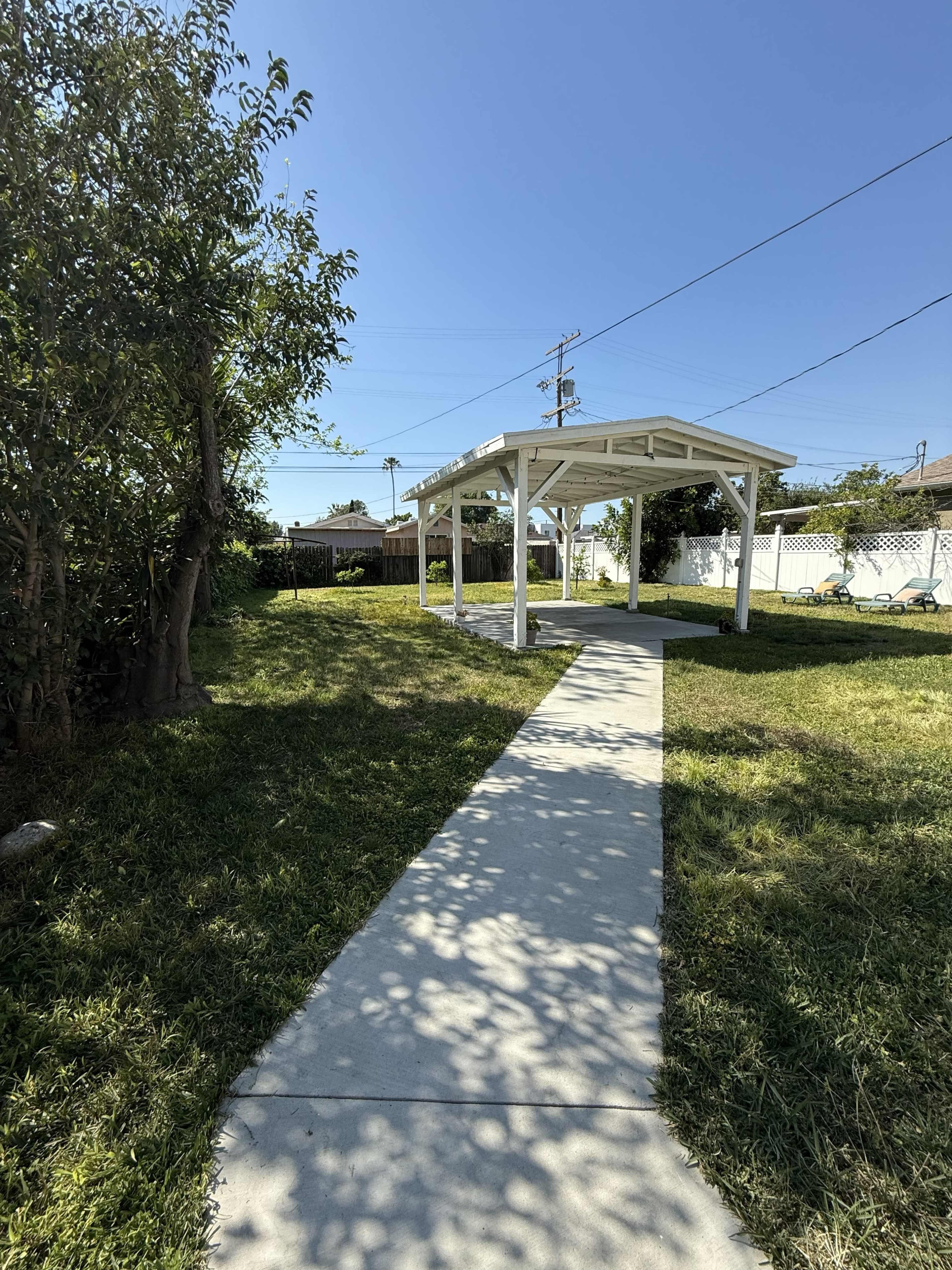 A concrete pathway leads to a white gazebo situated in a grassy yard under a clear blue sky.