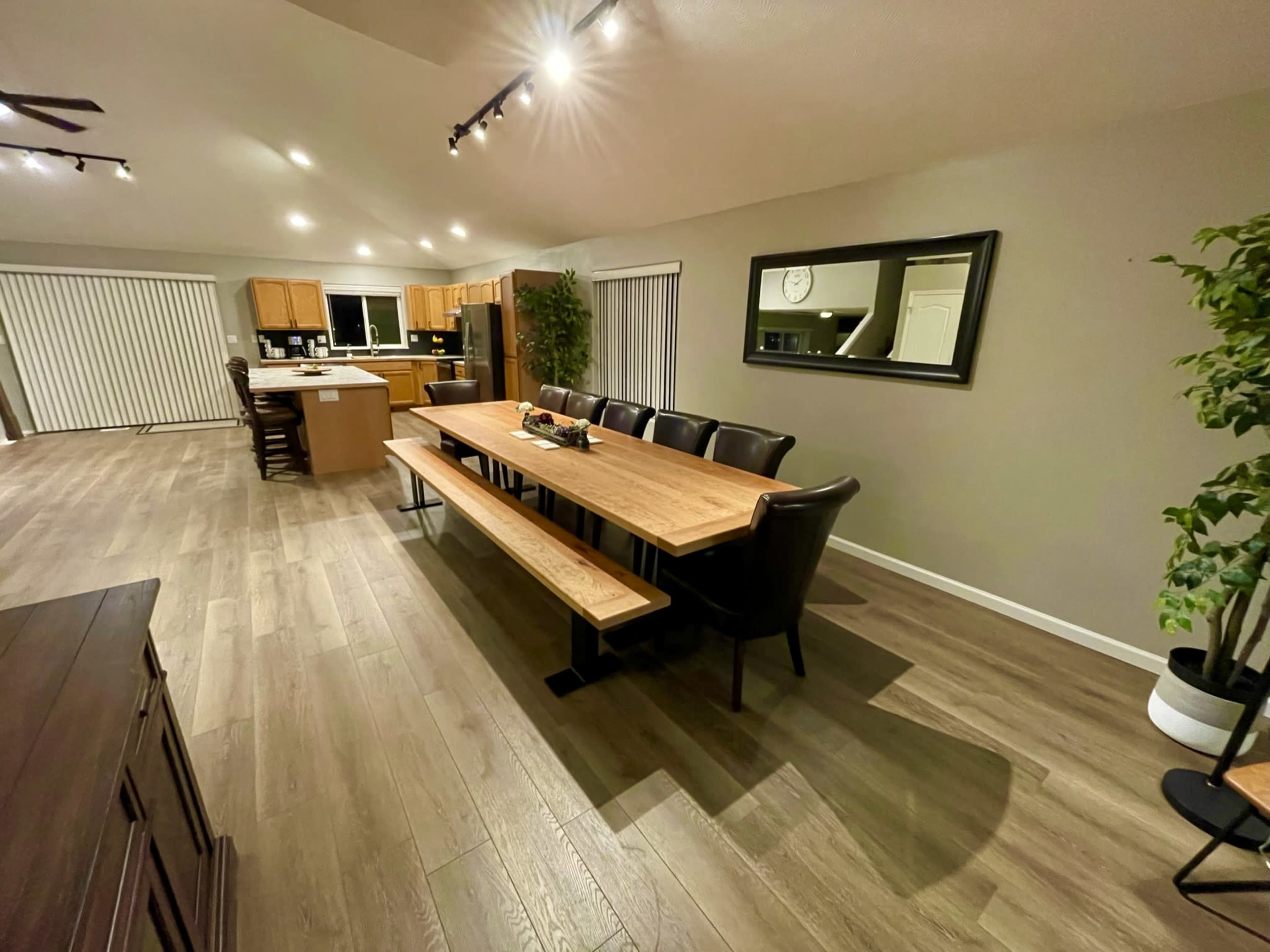 A spacious dining area with a long wooden table surrounded by black chairs, adjacent to a kitchen with light-colored cabinets.