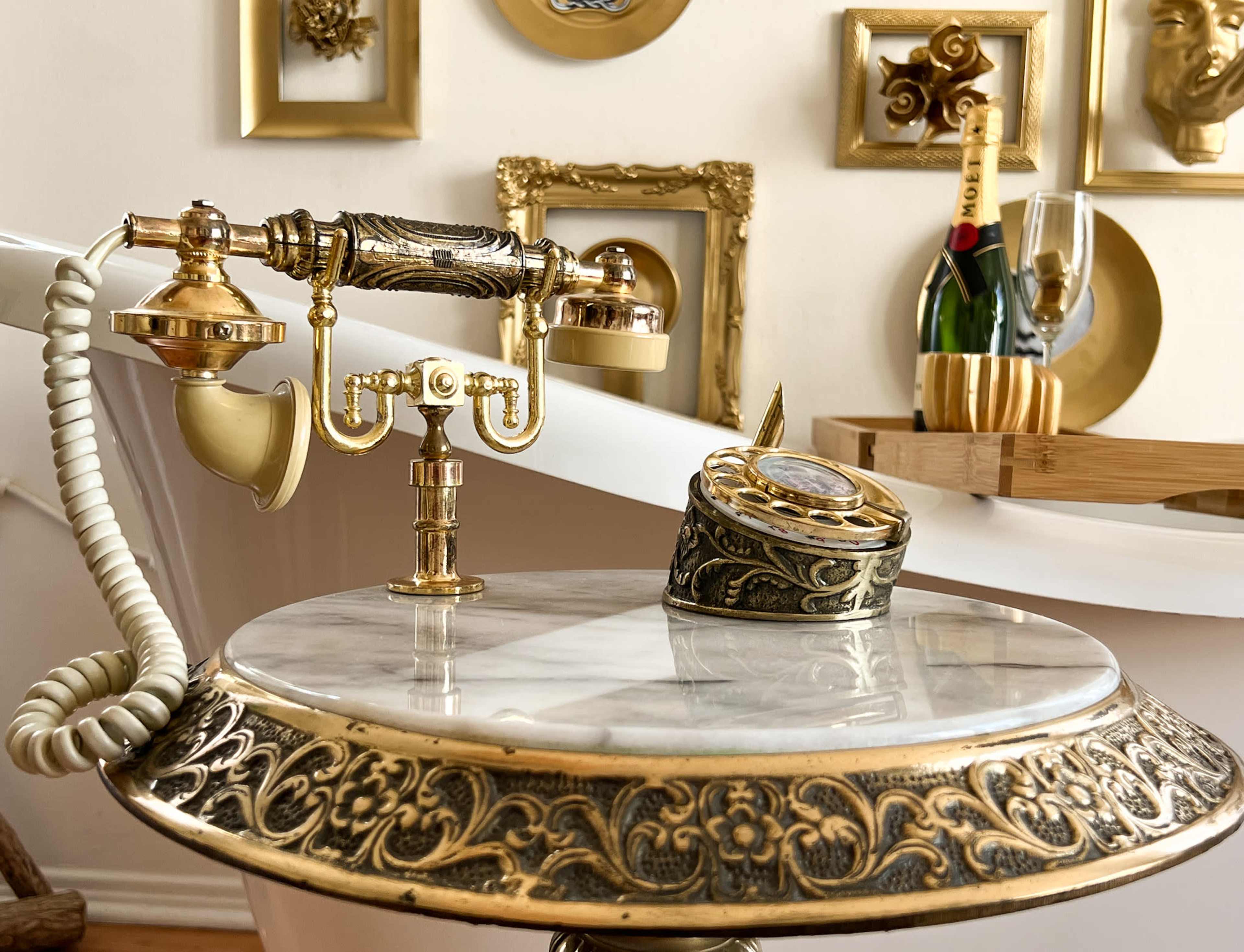 A vintage-style telephone and a decorative clock on a marble tabletop, surrounded by gold-framed artwork on the wall.