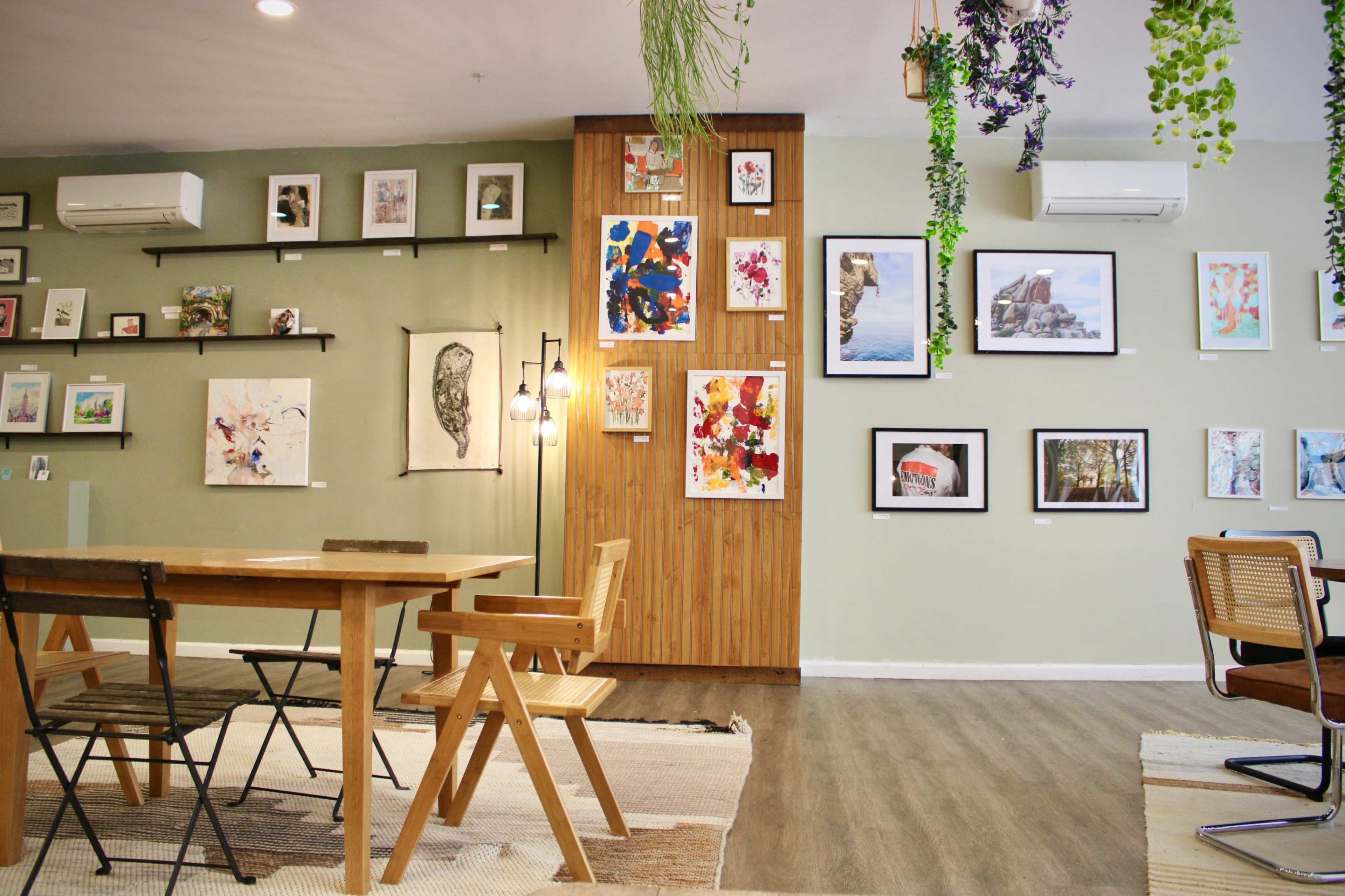 An art gallery with a wooden table and chairs, surrounded by various artworks displayed on the walls.