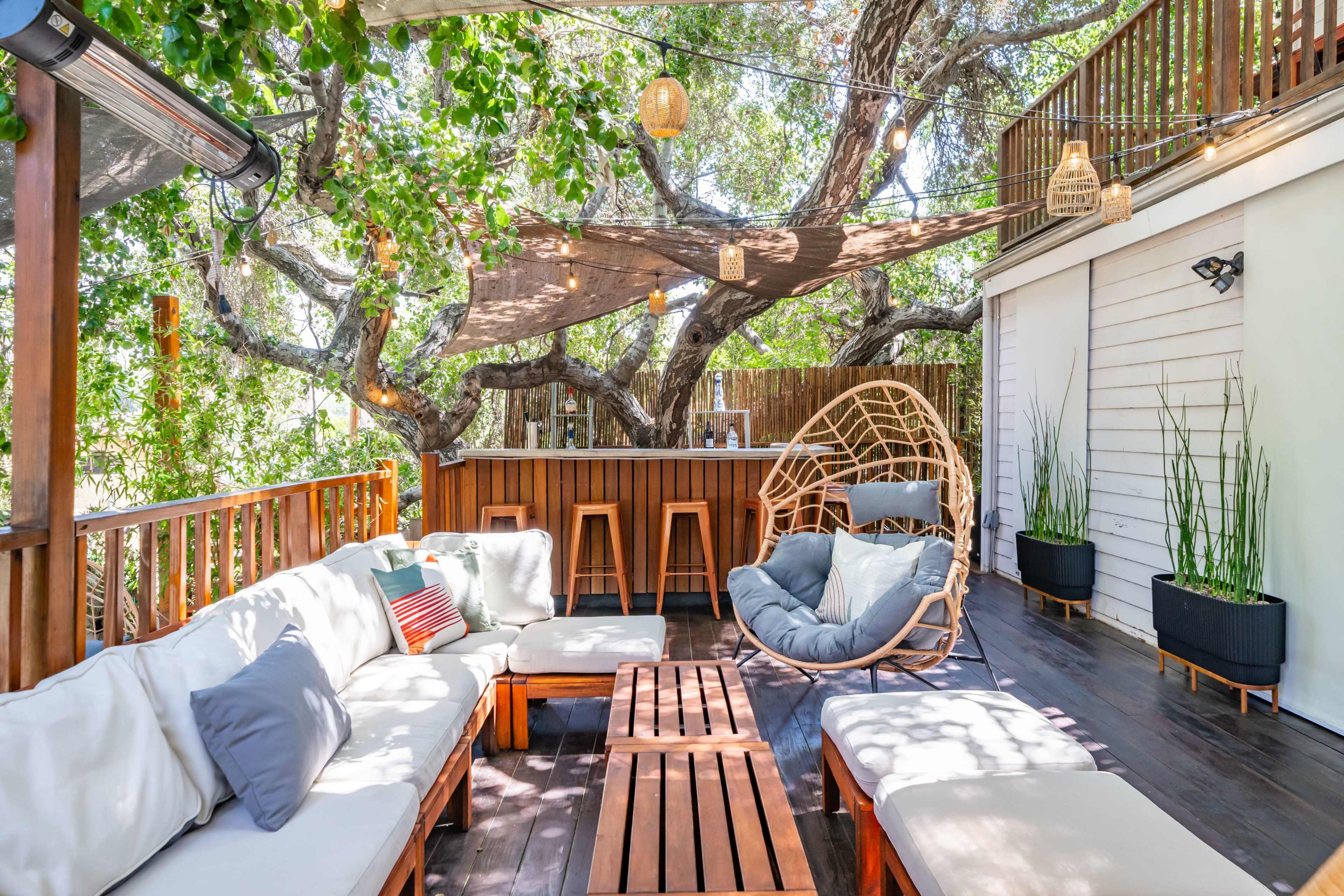 A spacious outdoor seating area features comfortable furniture, ambient lighting, and greenery, with a bar in the background.