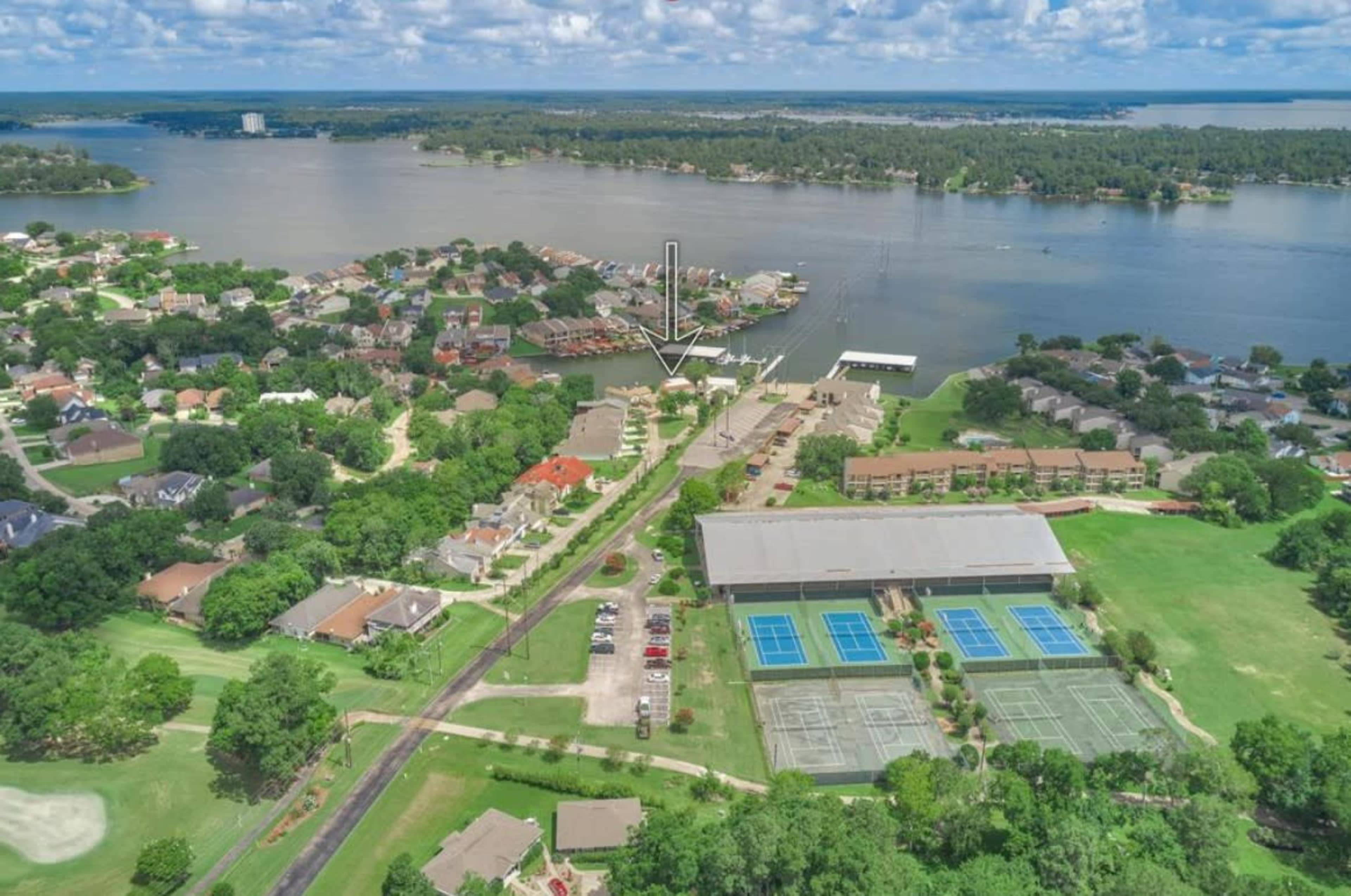 An aerial view of a lakeside community with residential homes, a marina, and tennis courts adjacent to a large building.