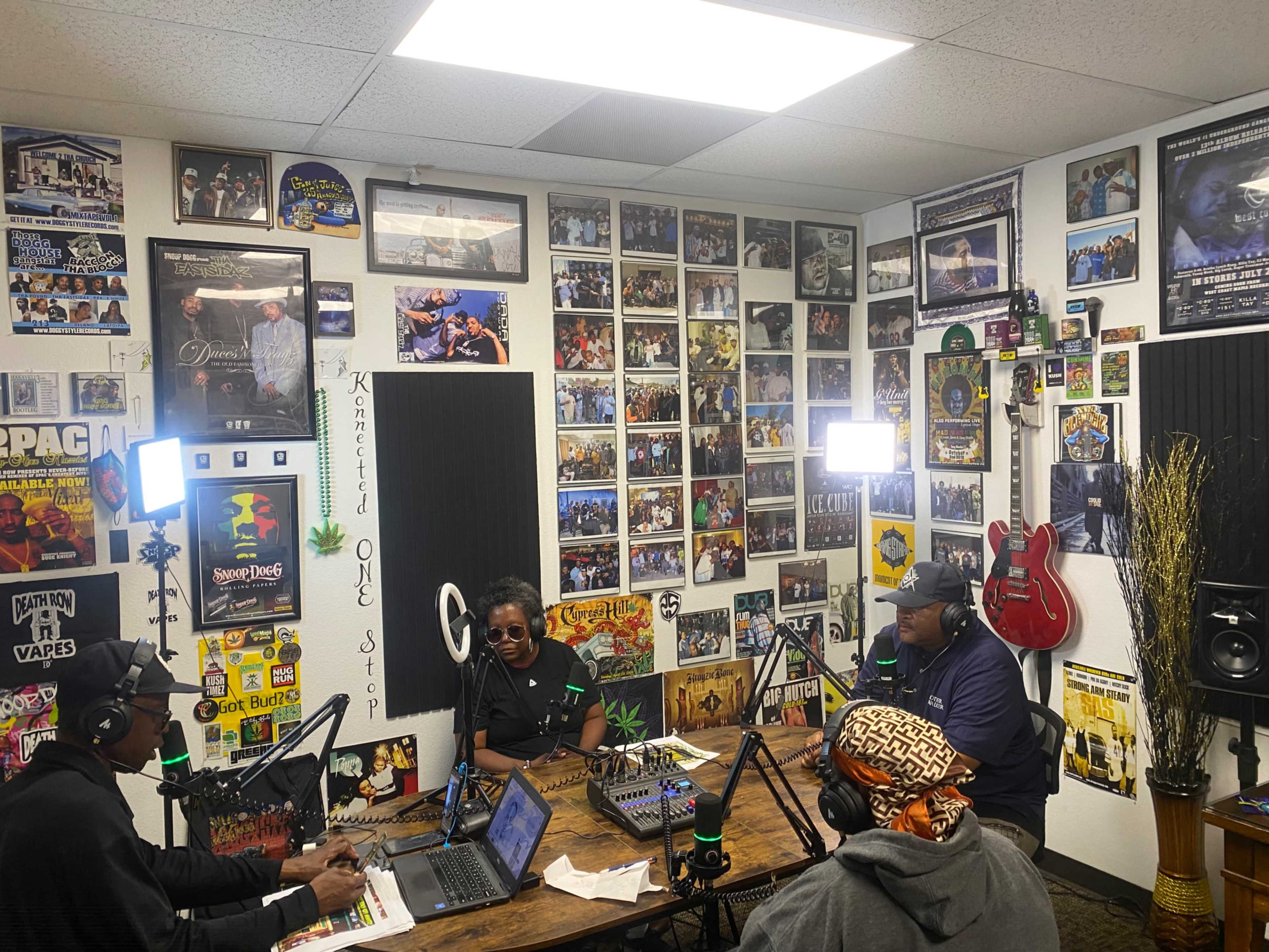 A group of three people participates in a podcast recording in a room decorated with numerous framed photos and posters.