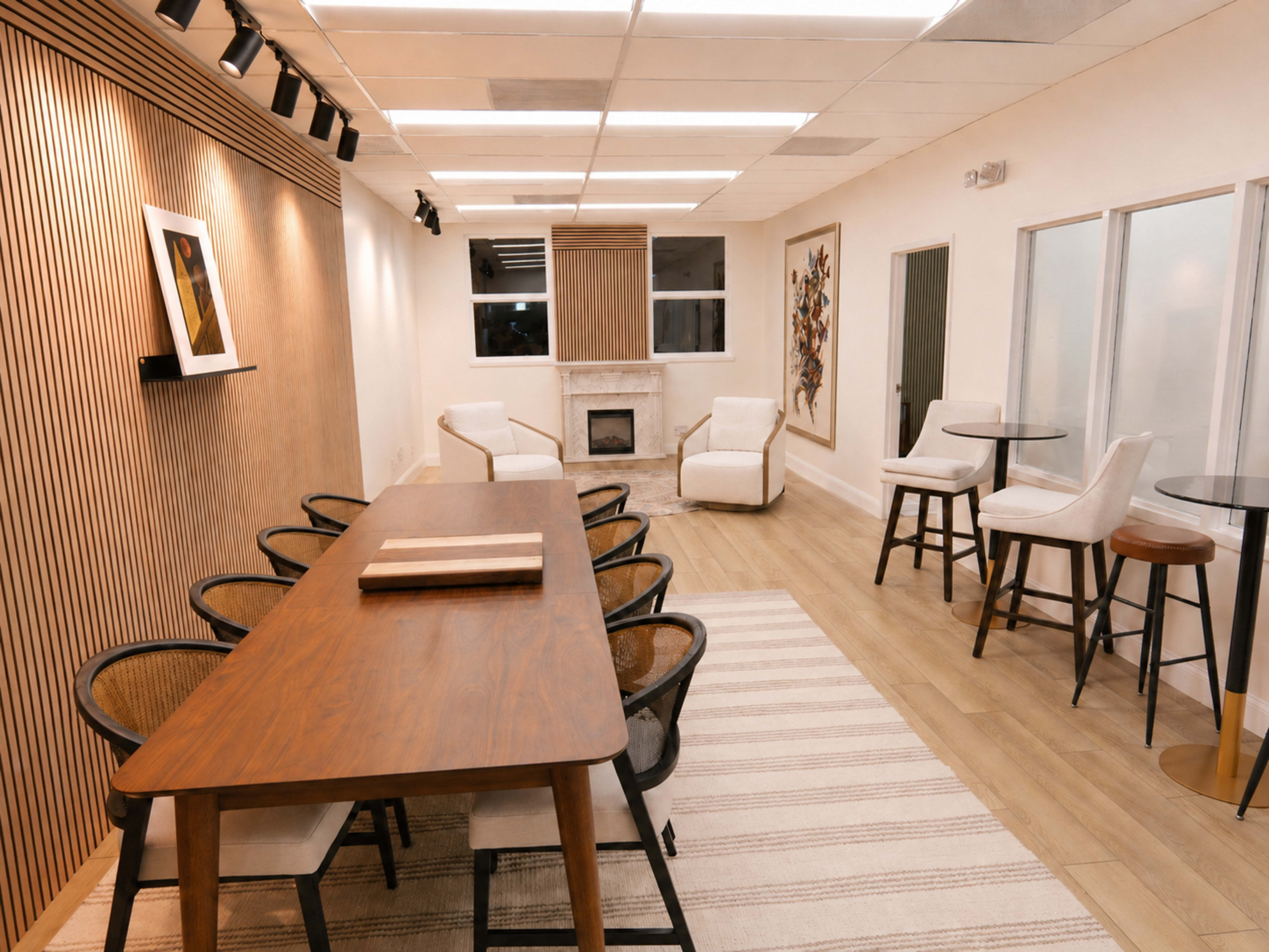 The image shows a modern meeting room with a large wooden table surrounded by chairs, a cozy seating area with two armchairs, and a small fireplace.