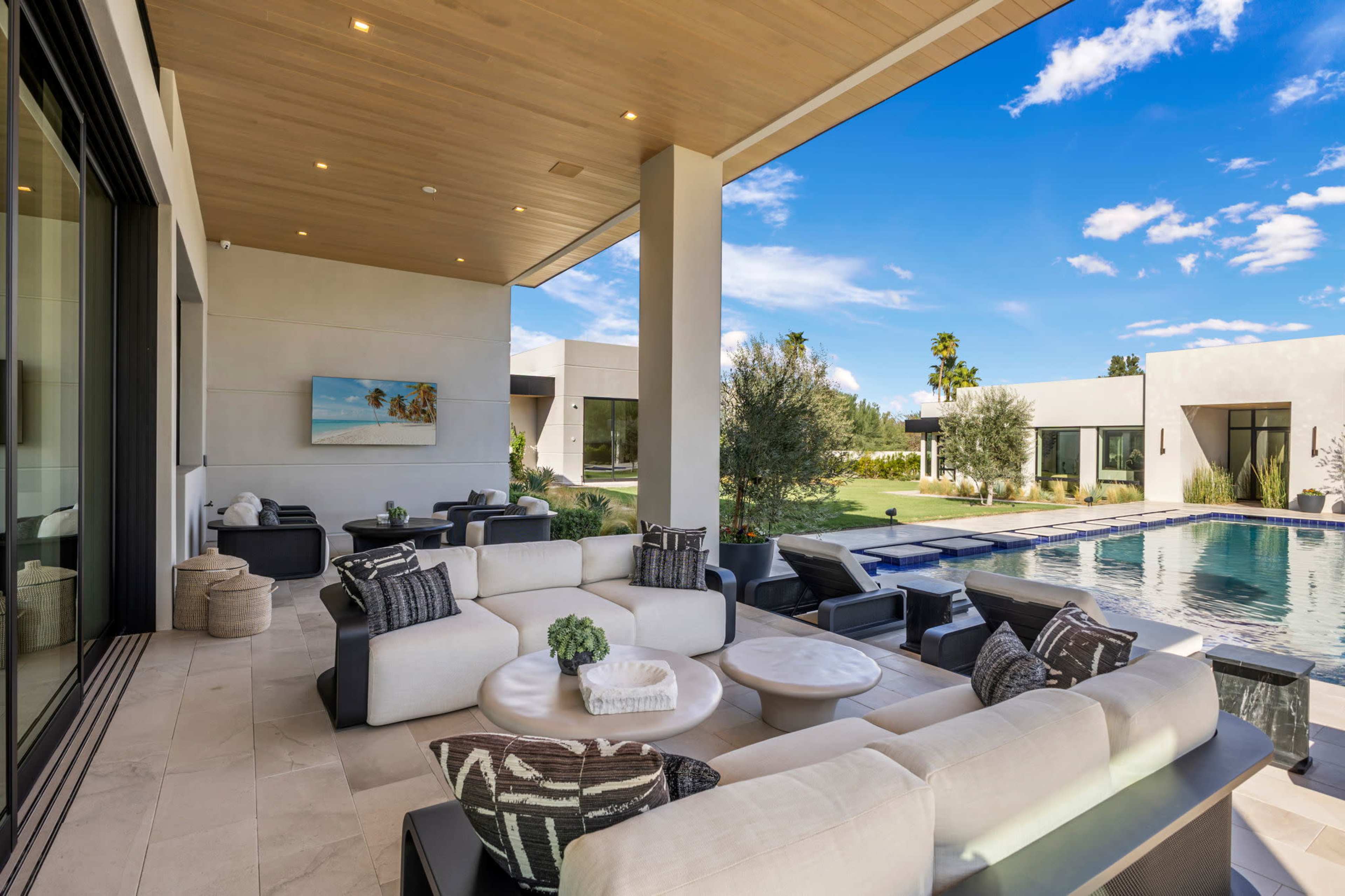 A modern outdoor lounge area features comfortable seating arrangements and a view of a swimming pool surrounded by landscaped gardens.
