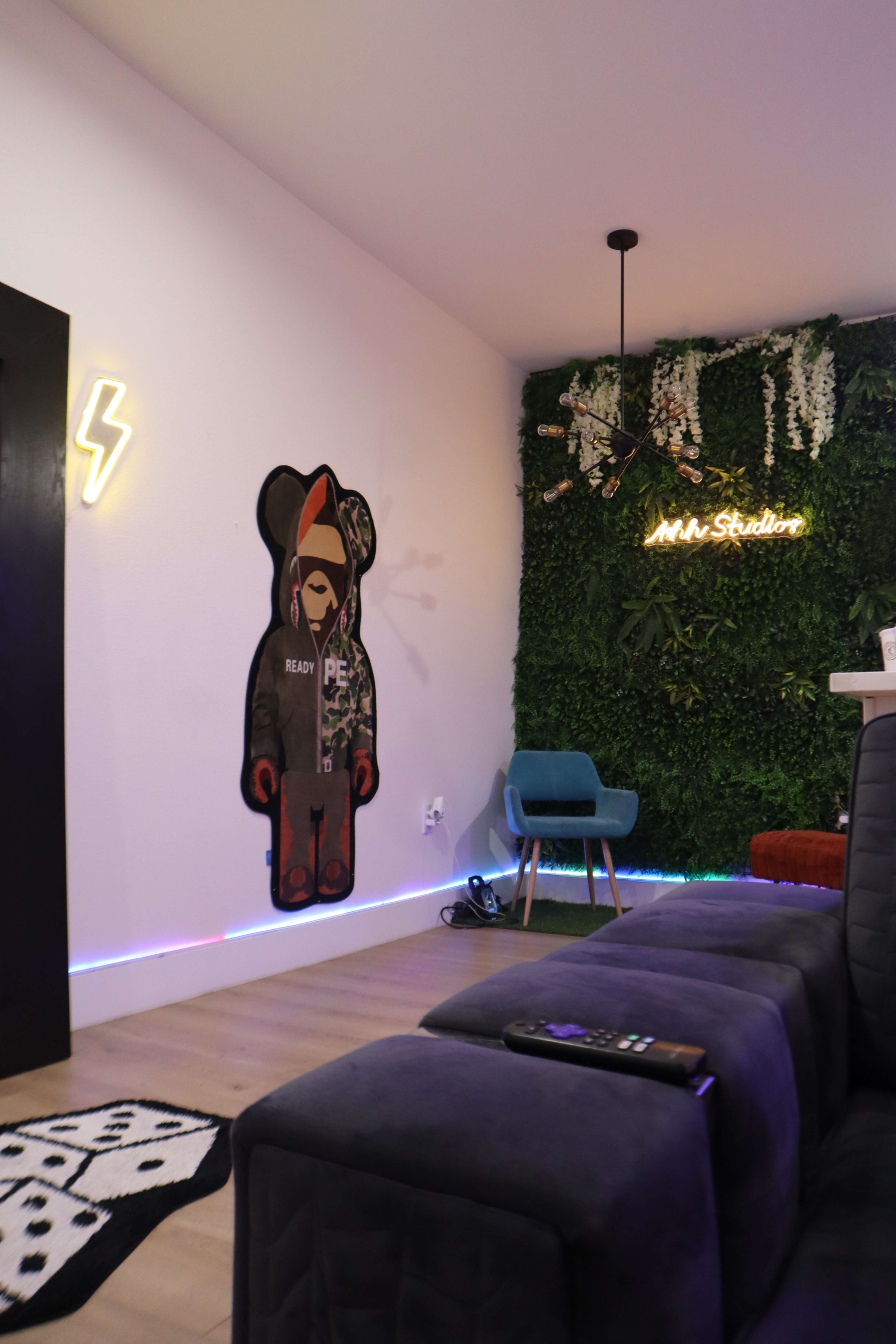 The image shows a modern, interior space featuring a plush gray couch, a blue chair, a wall adorned with greenery, and a large bear-shaped art piece.