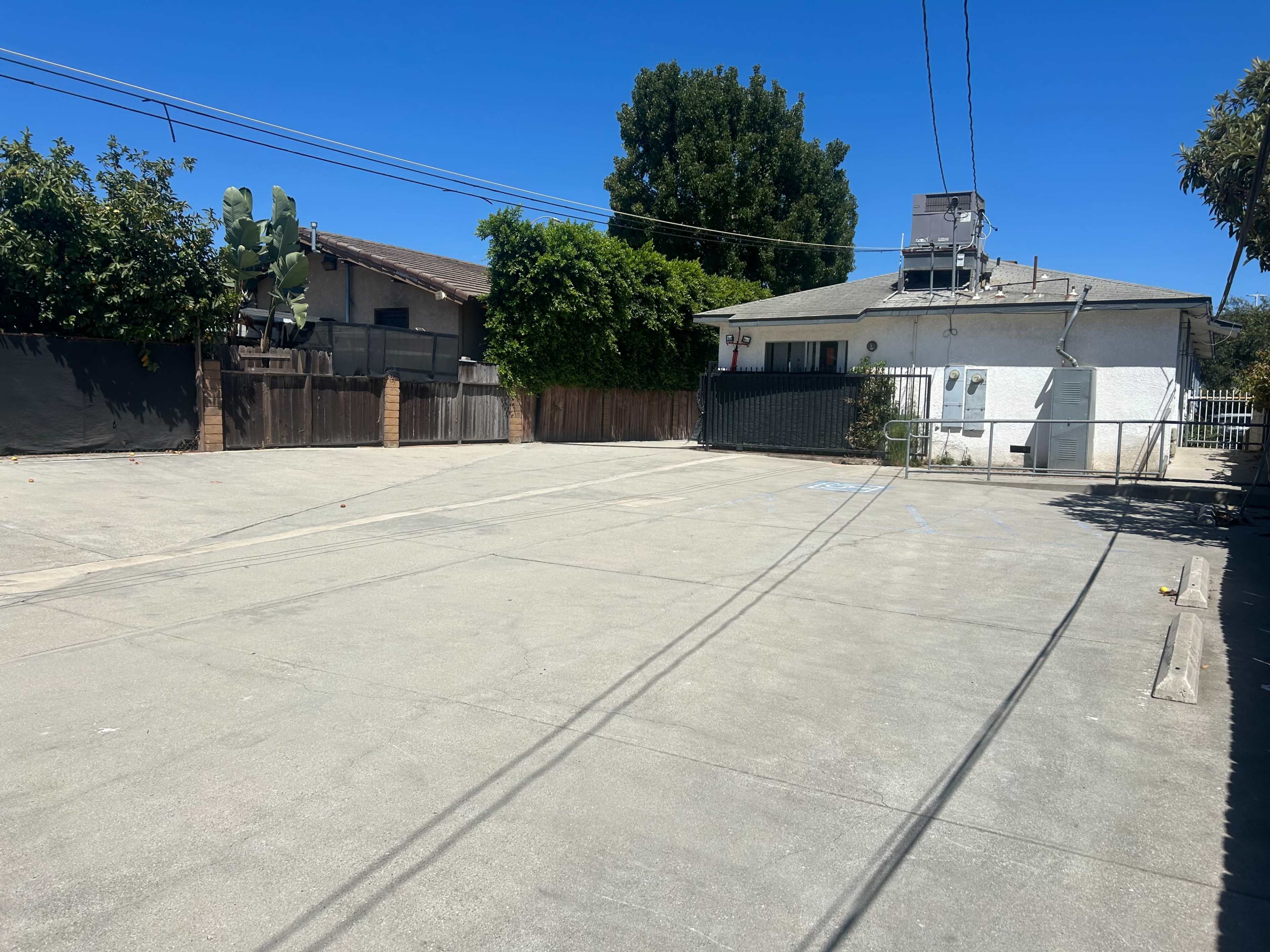 The image shows a vacant, paved area with a building and some trees in the background.